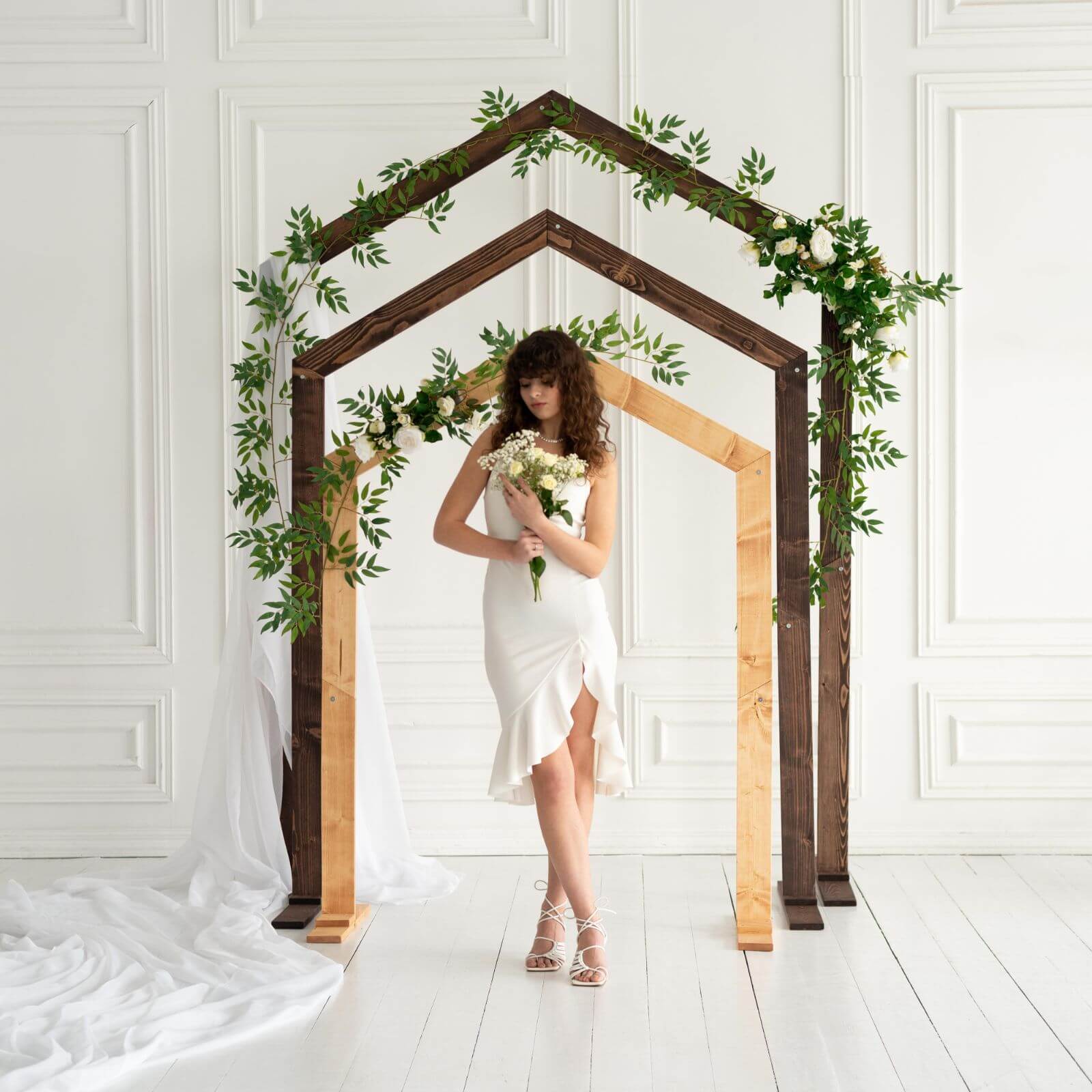 Bride posing with bouquet under layered wooden pentagon wedding arches.