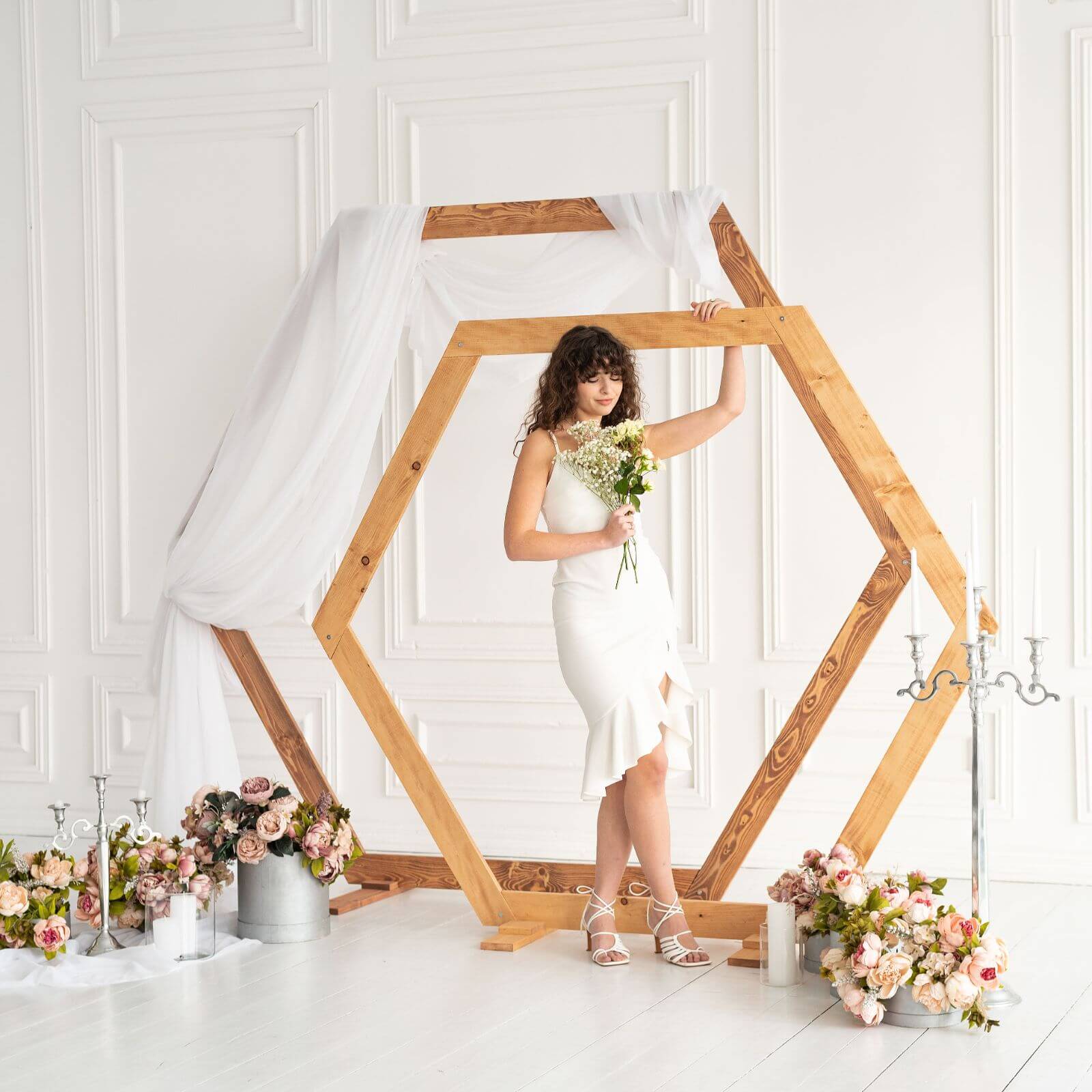 Bride holding bouquet inside rustic wooden hexagon wedding arch.