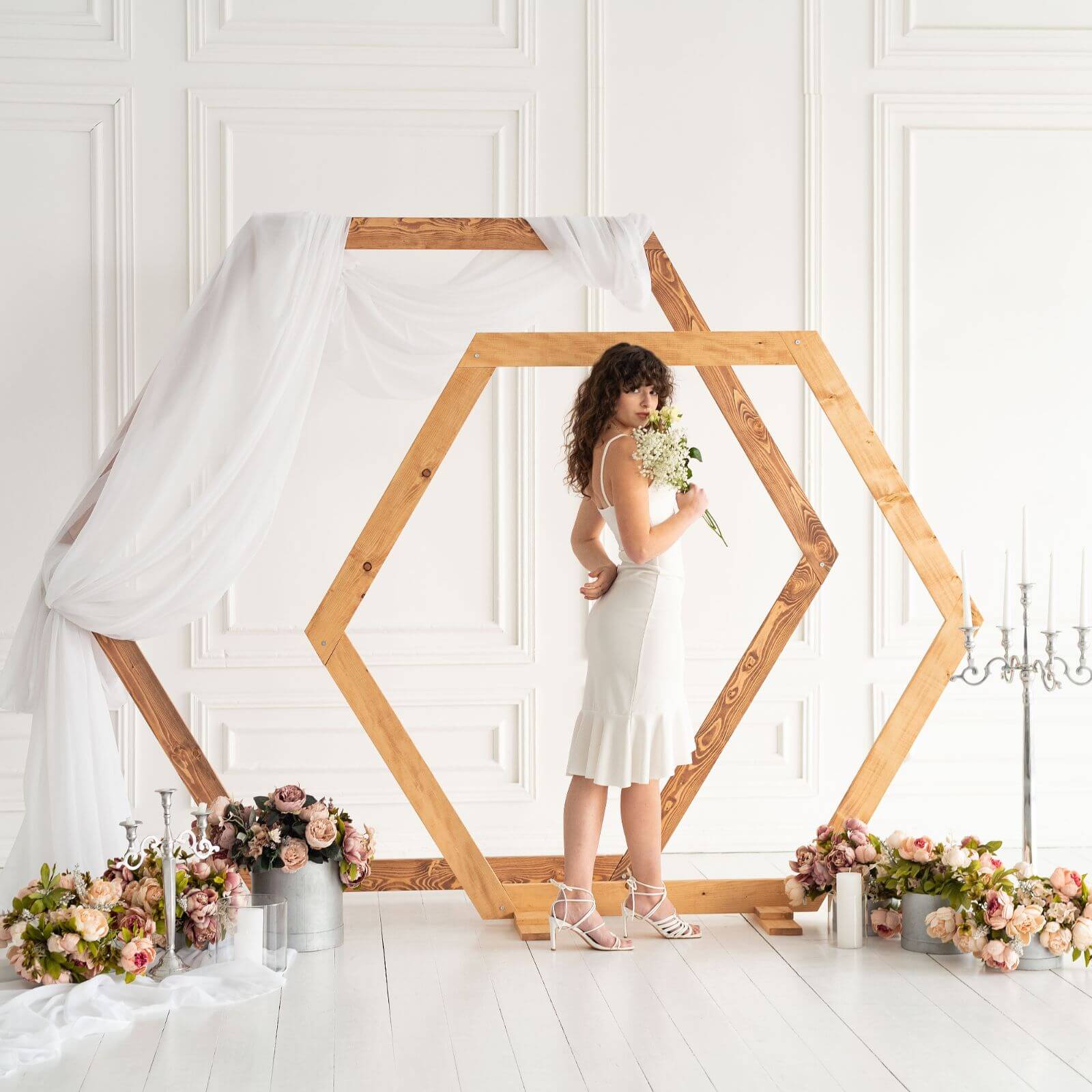 Bride posing inside wooden hexagon wedding arch with flowers.