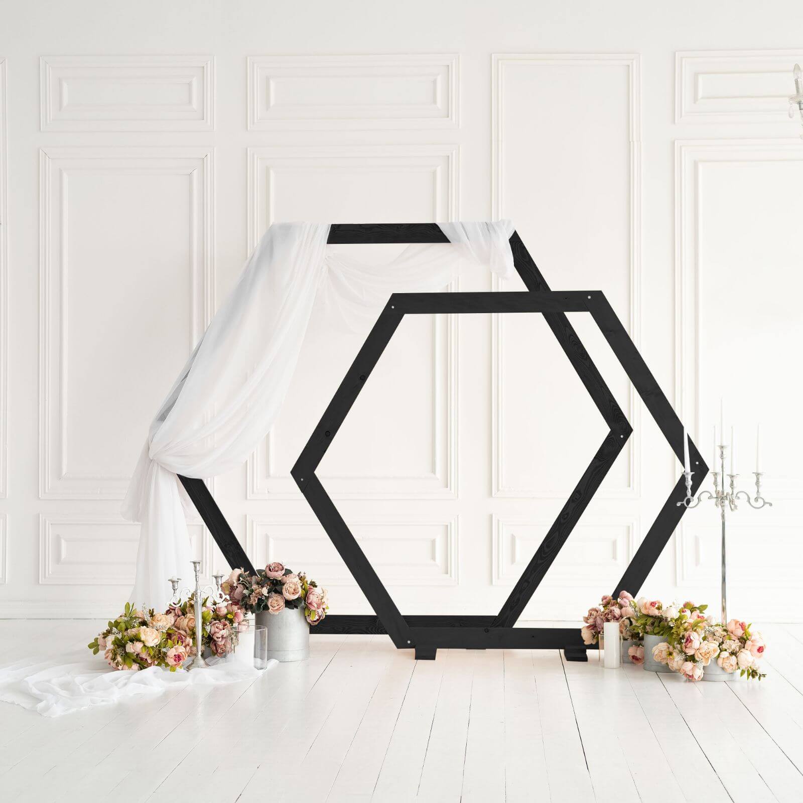 Black hexagon wedding arch decorated with white drapery fabric.