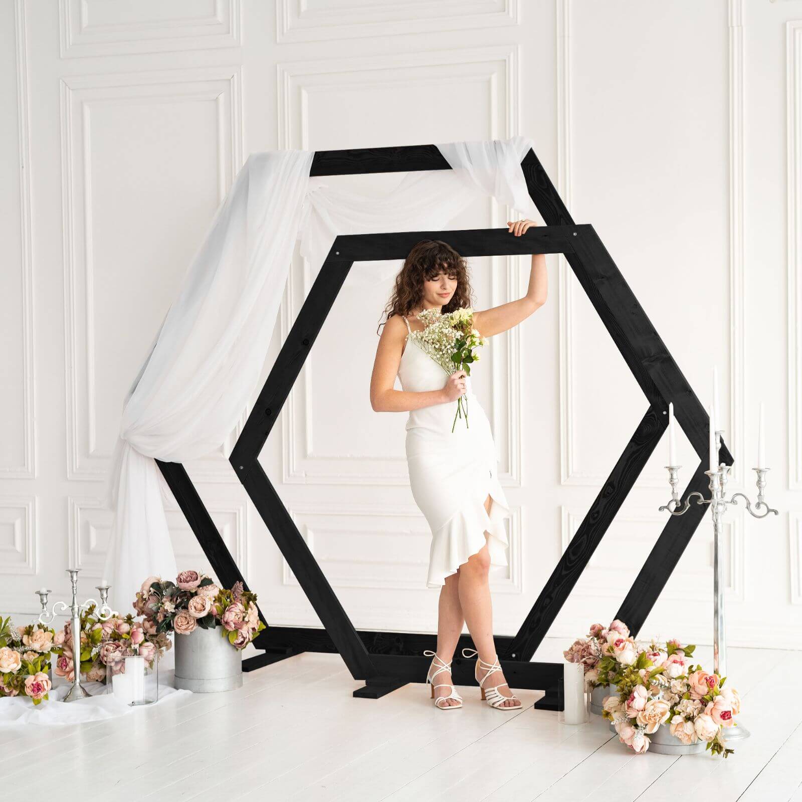Elegant bride posing with bouquet under black hexagon arch.