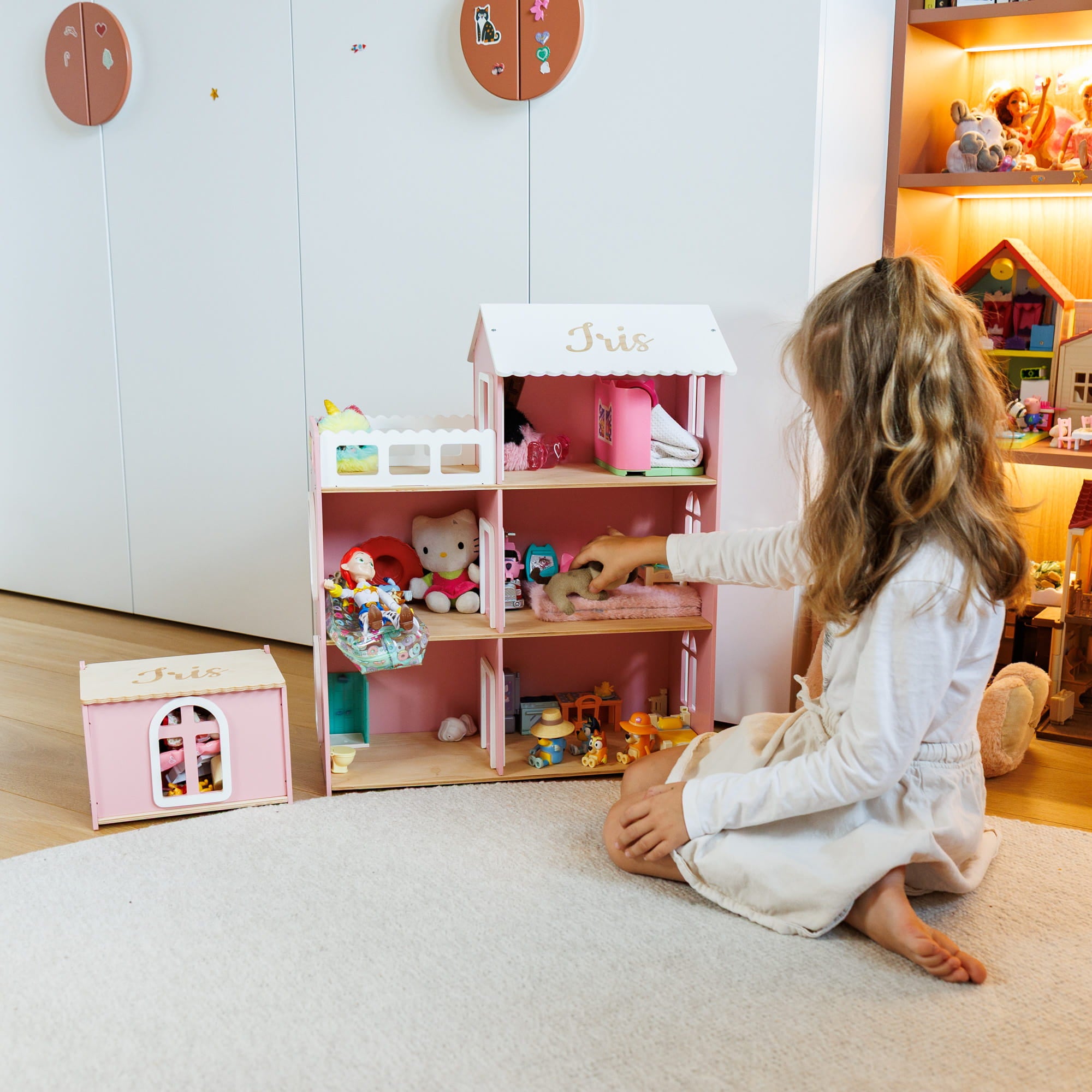a pink wooden dollhouse with furniture and toys inside