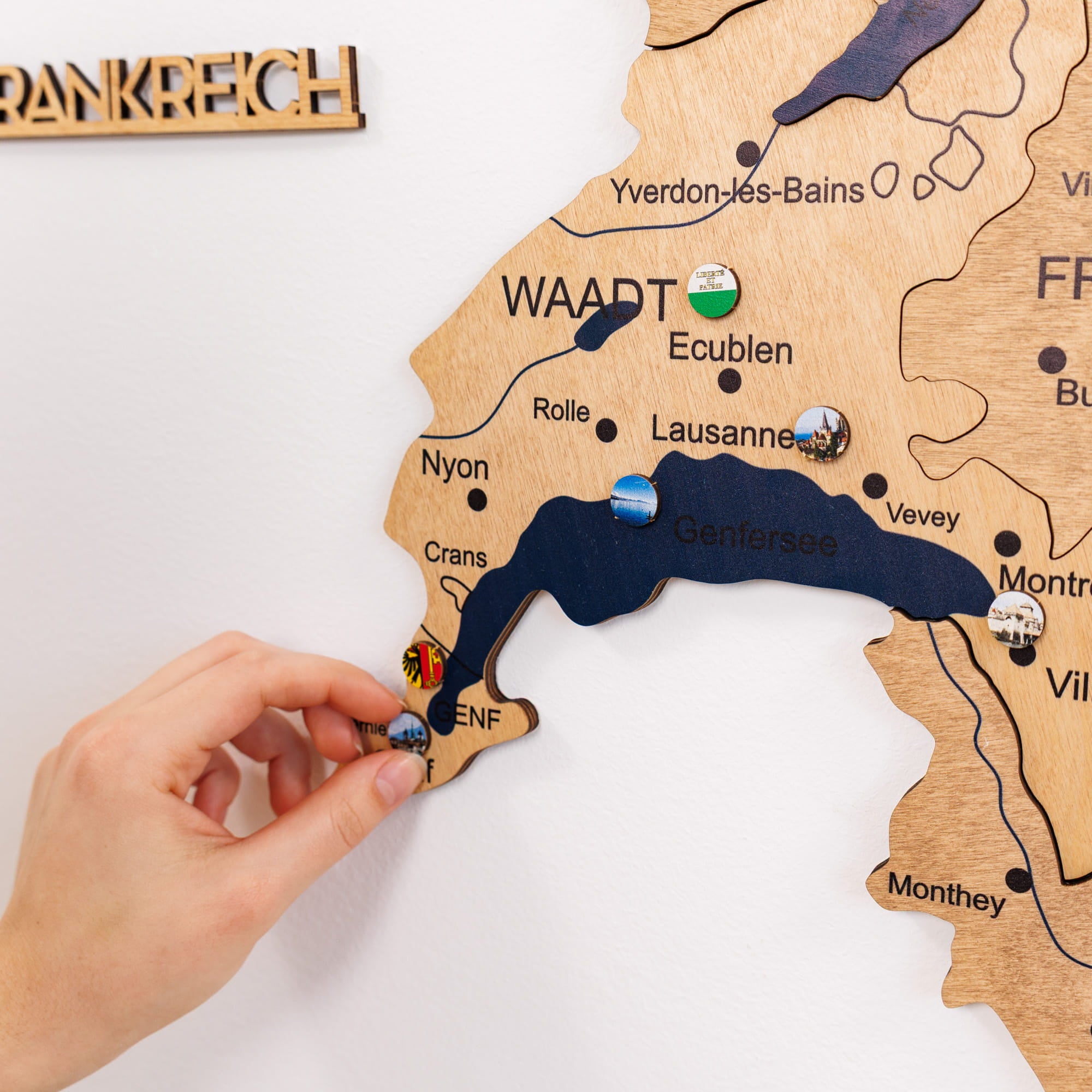 Wooden map of Switzerland with a hand placing a small flag on it