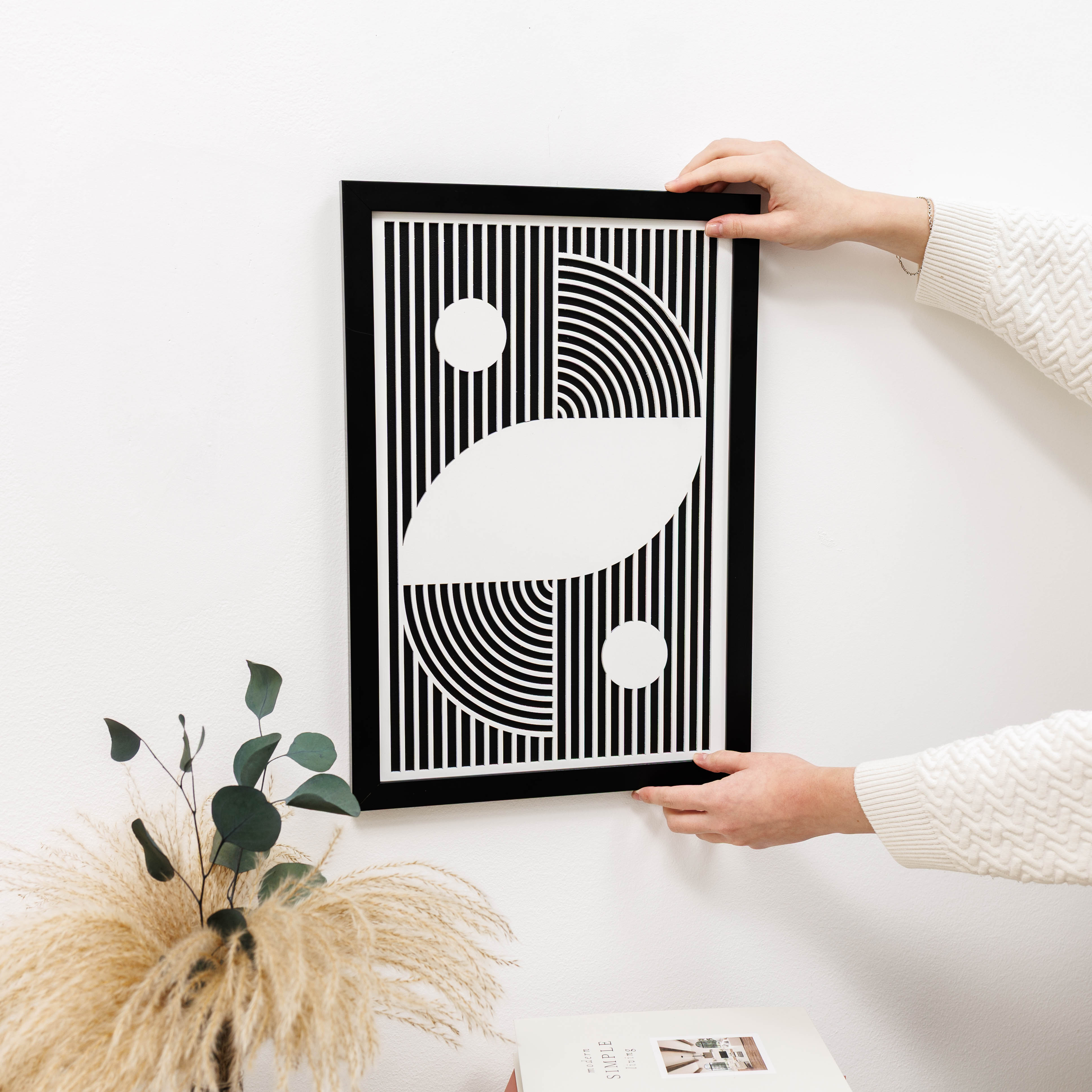 Person holding a framed abstract art print with geometric shapes on a white surface.