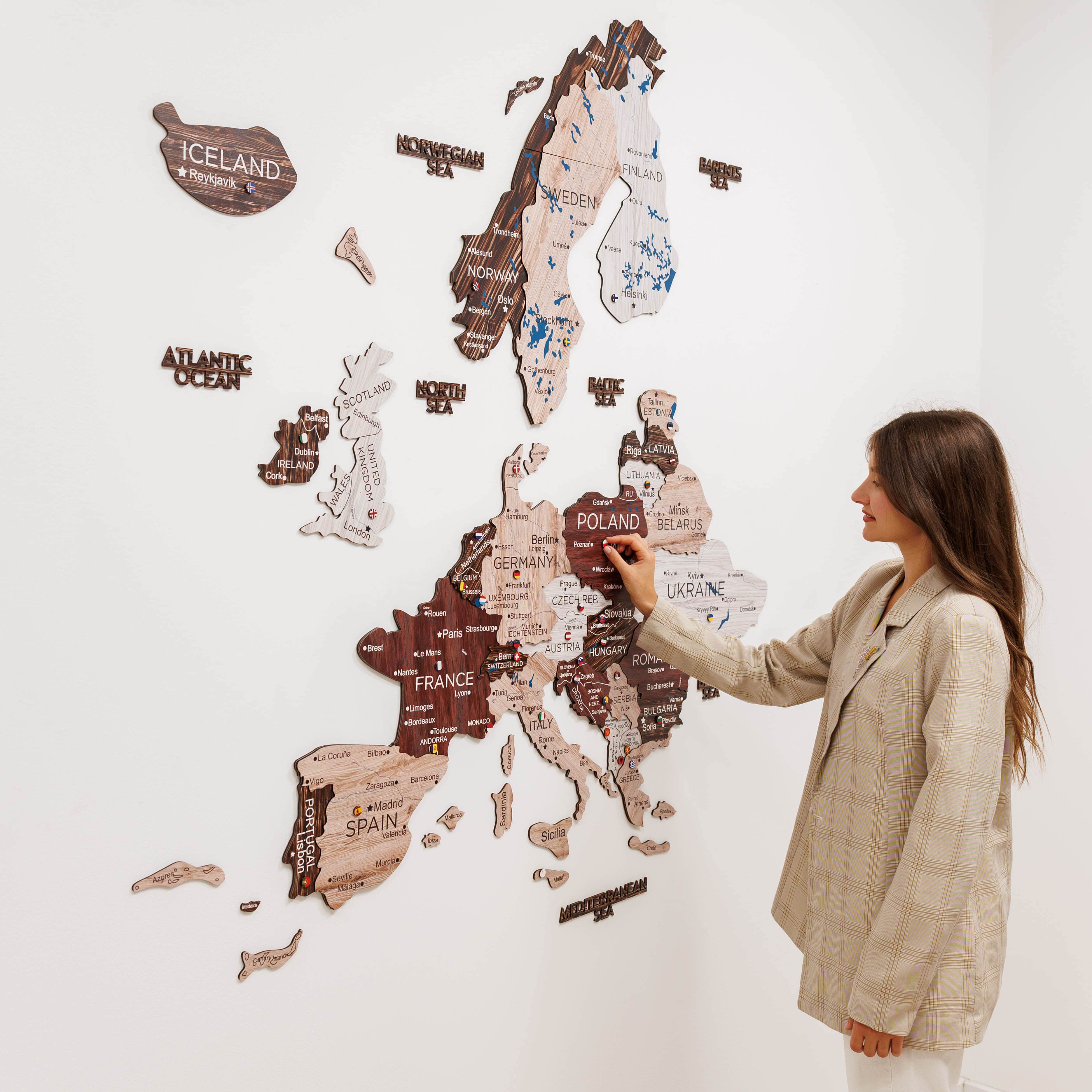 Woman interacting with a wall-mounted wooden map of Europe on a white wall.