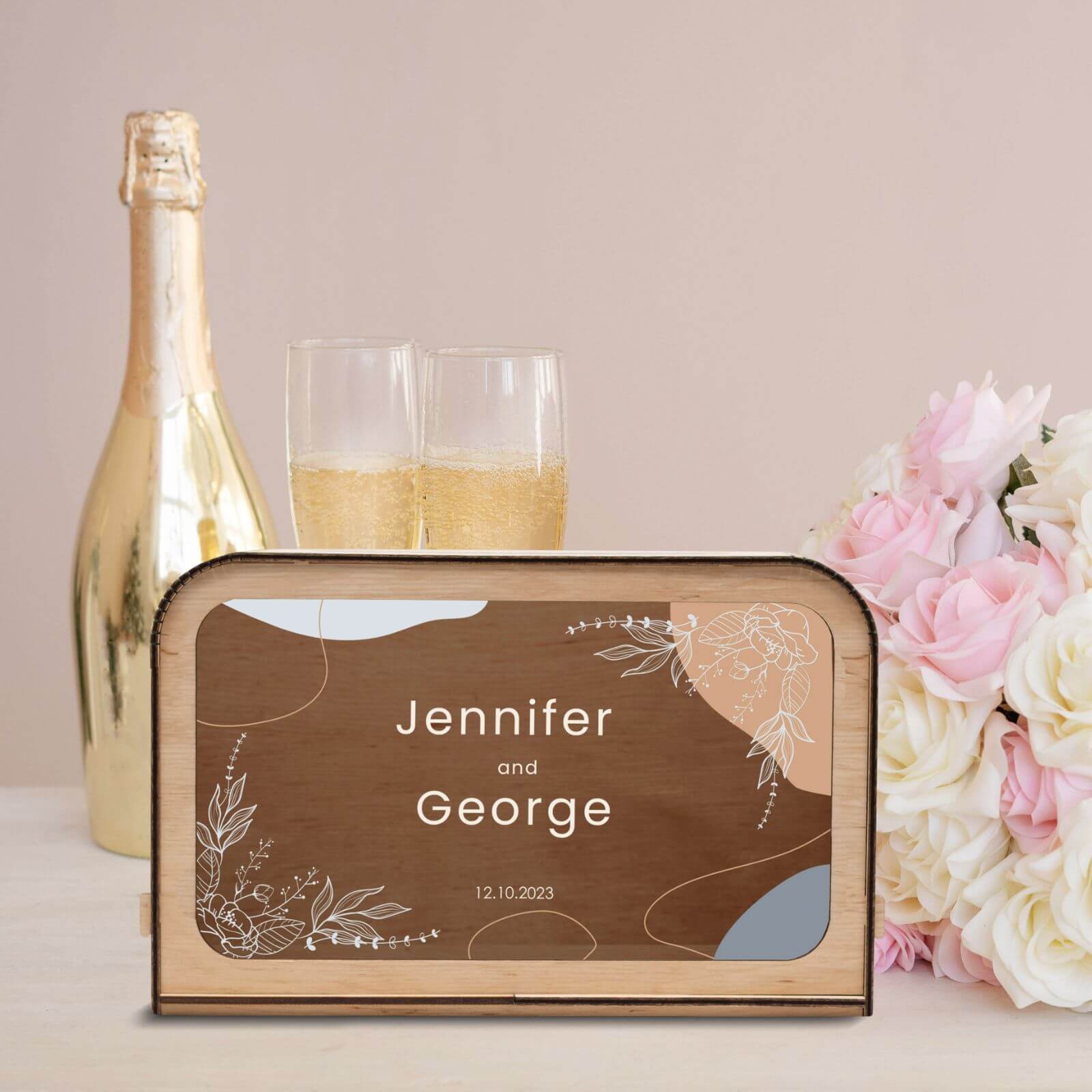 Personalized wooden wedding card box with engraved names Jennifer and George, champagne and flowers in background