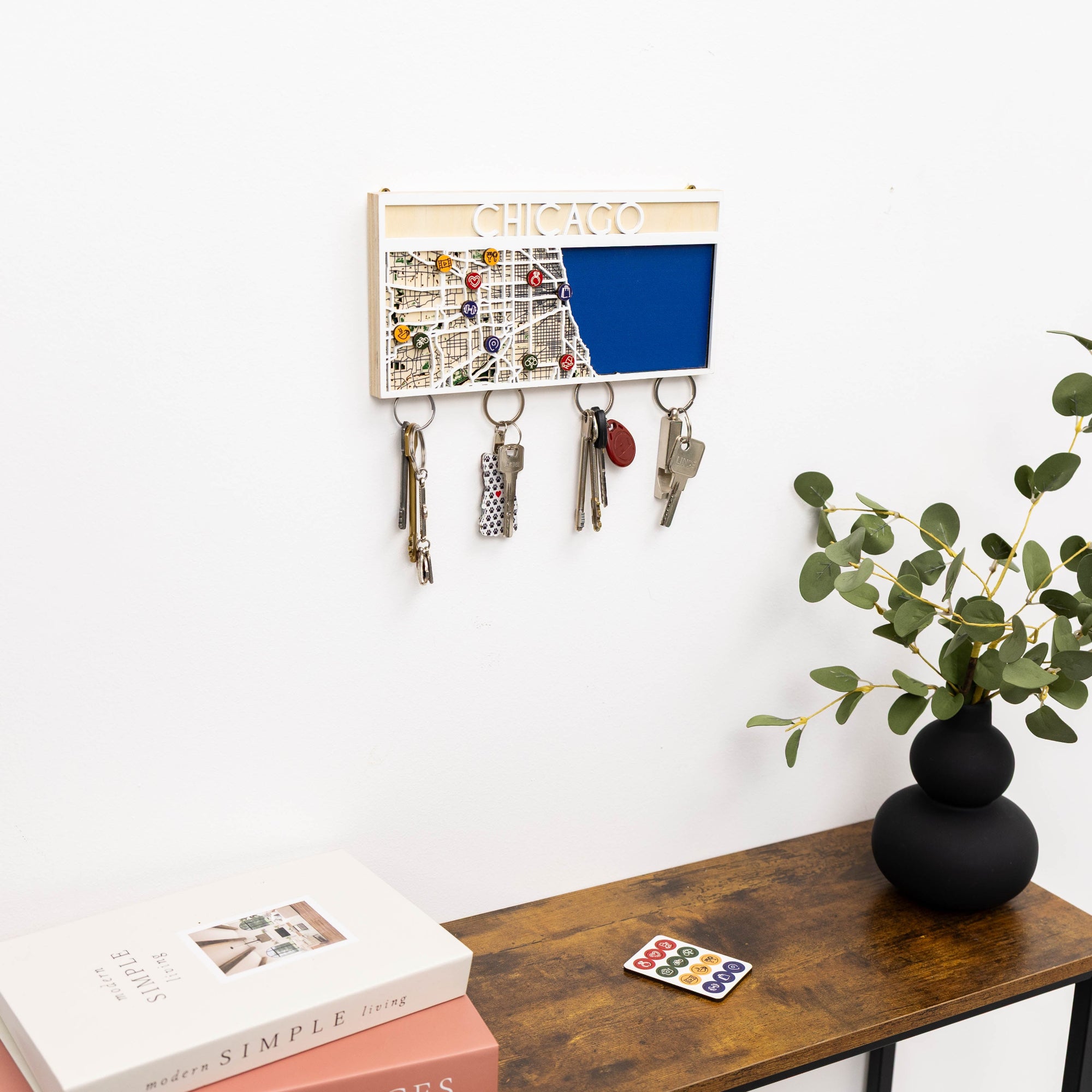 Key holder with keys on a wall above a wooden bench with books and a plant.