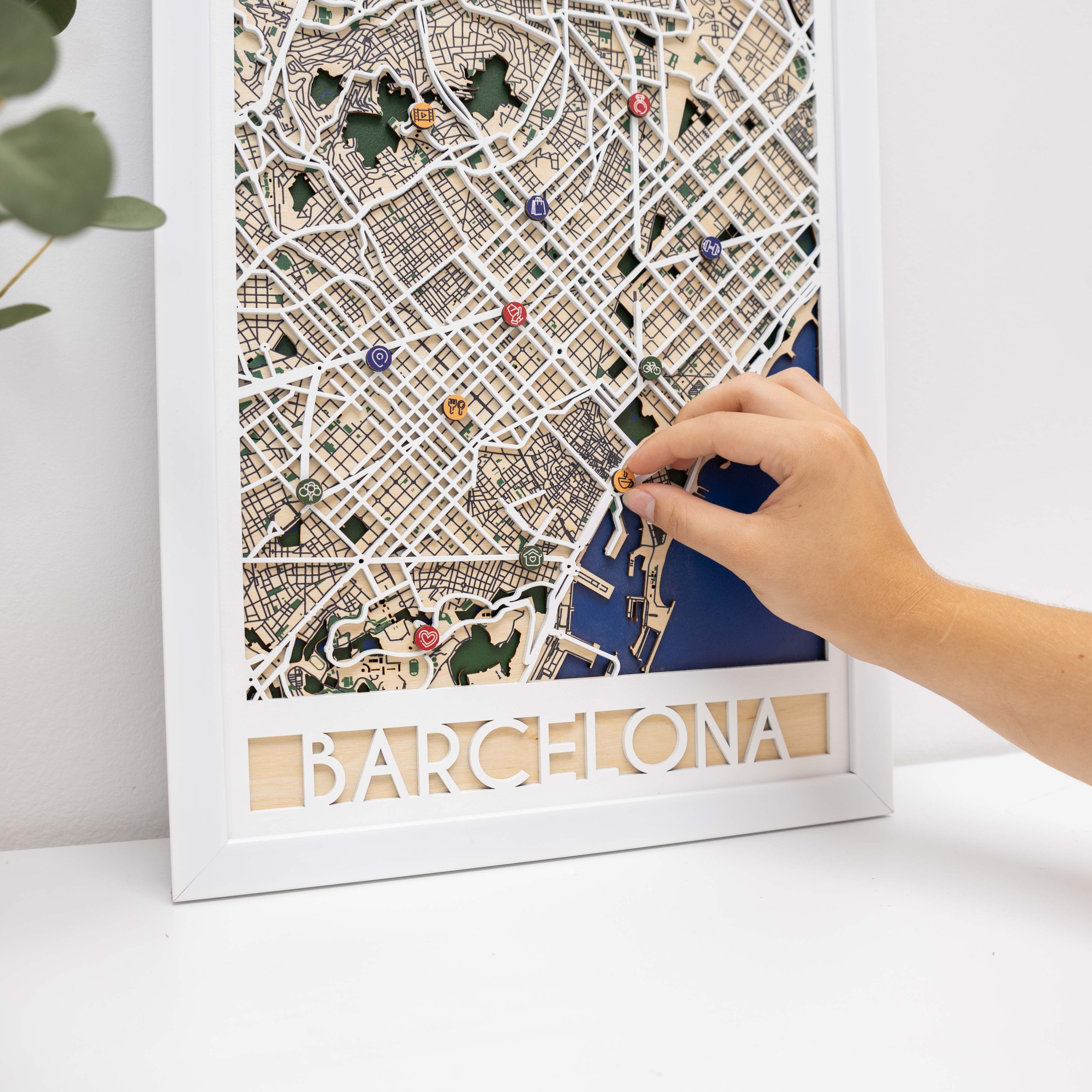 Framed map of Barcelona with a hand adjusting a piece on a white surface.