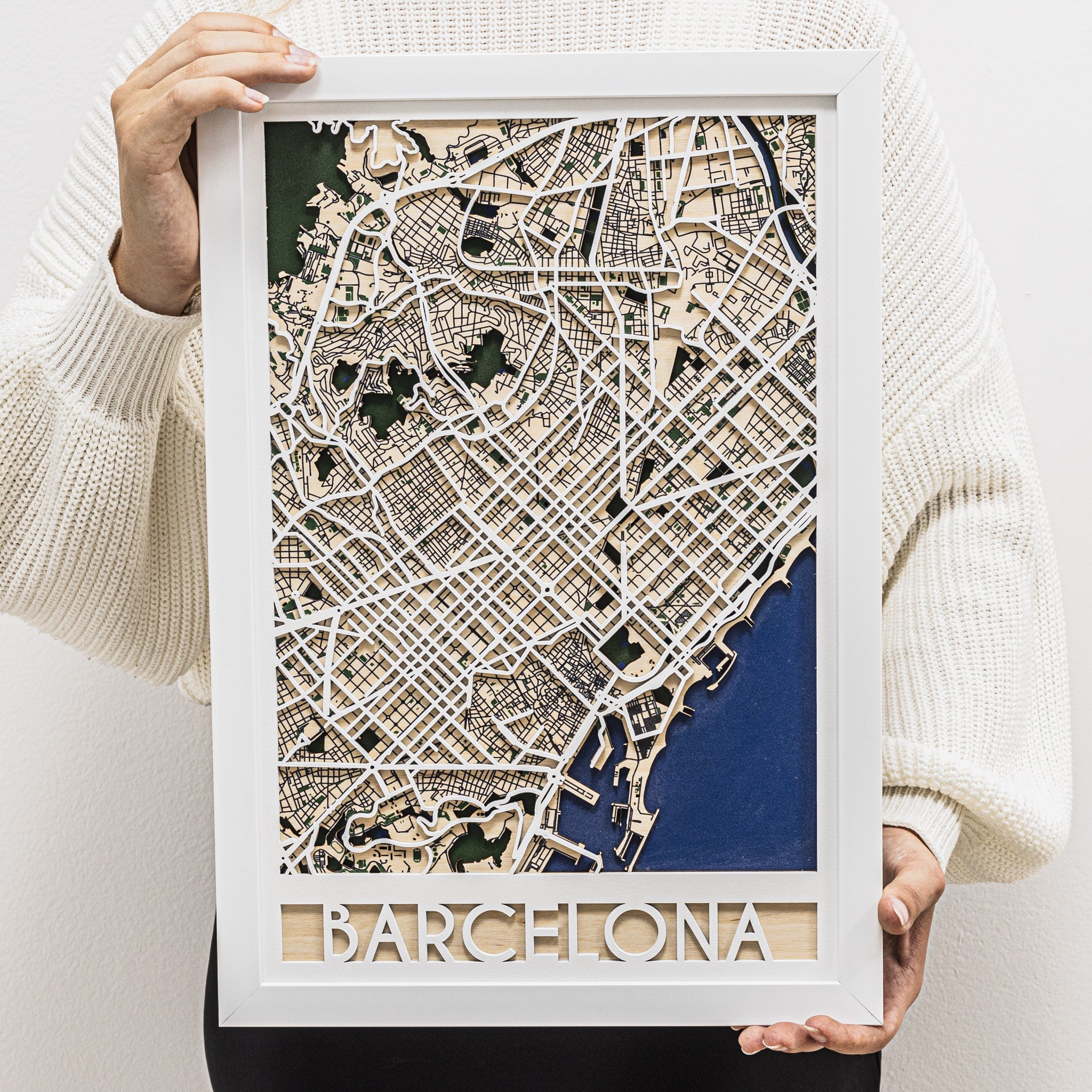Framed map of Barcelona held by a person wearing a white sweater.