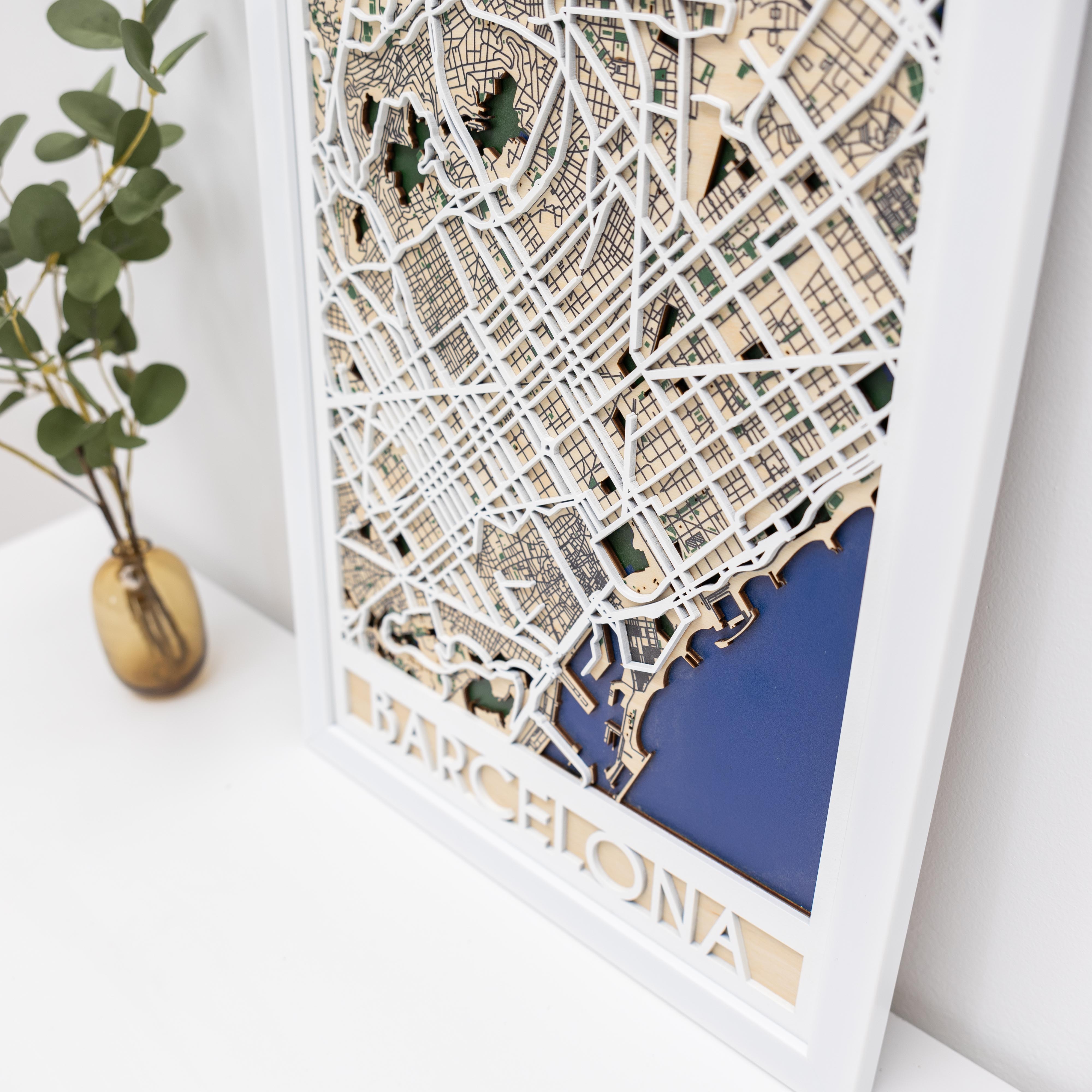 Framed cut-out map of Barcelona on a white surface with a plant in the background