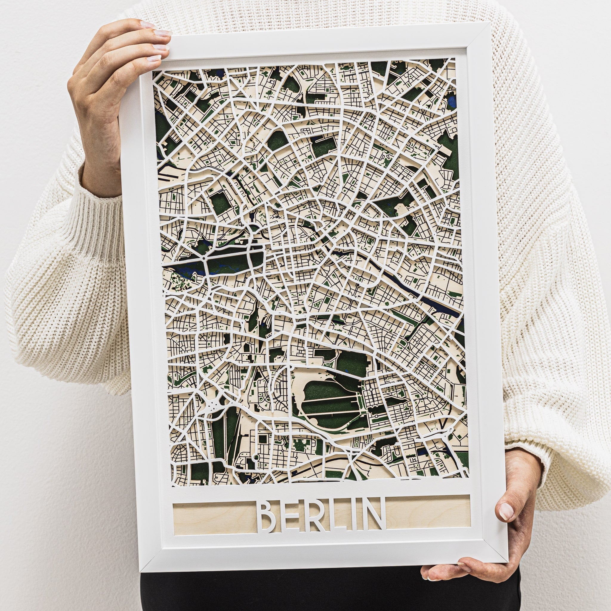 Framed map of Berlin held by a person wearing a white sweater.