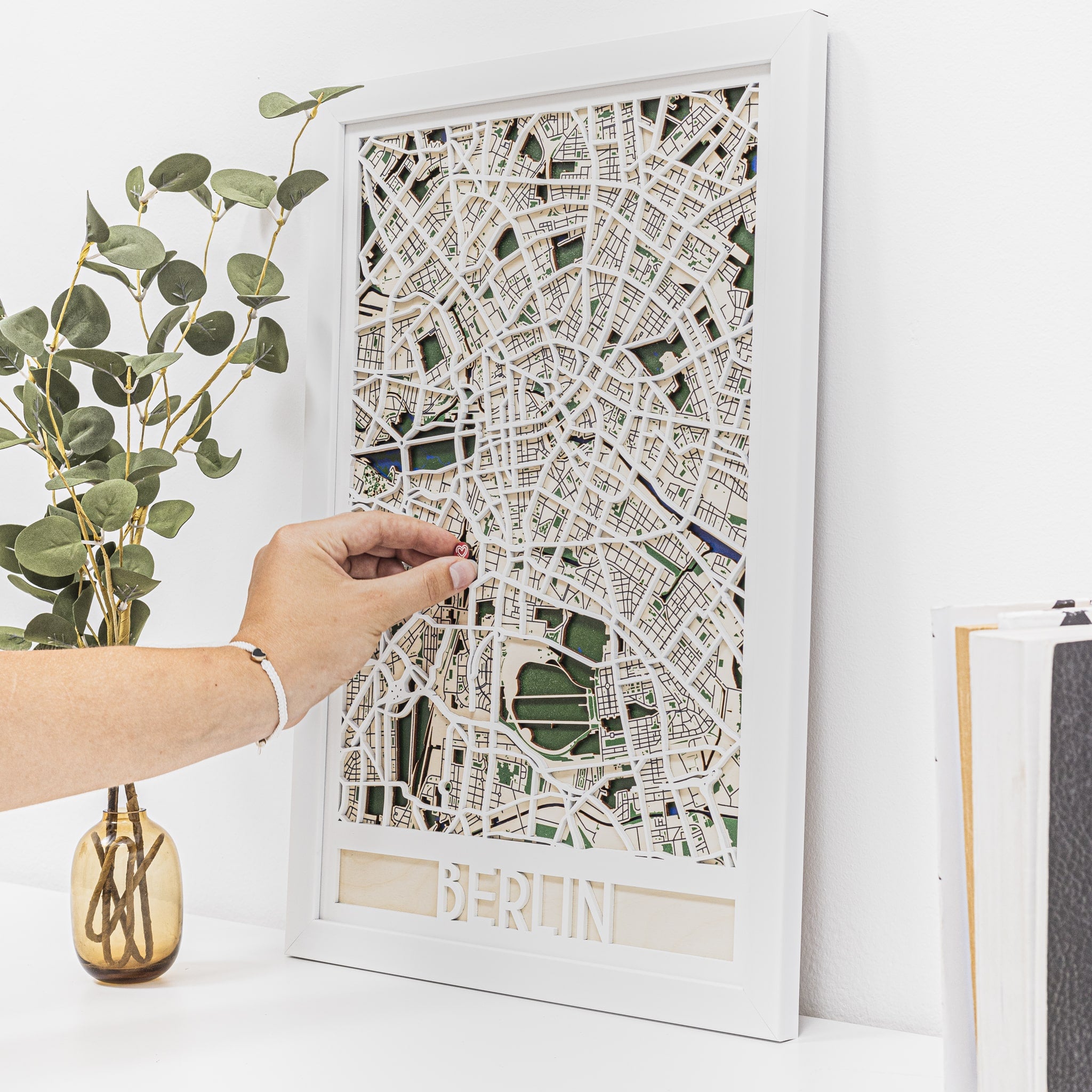 Framed city map of Berlin on a white surface with a hand touching it