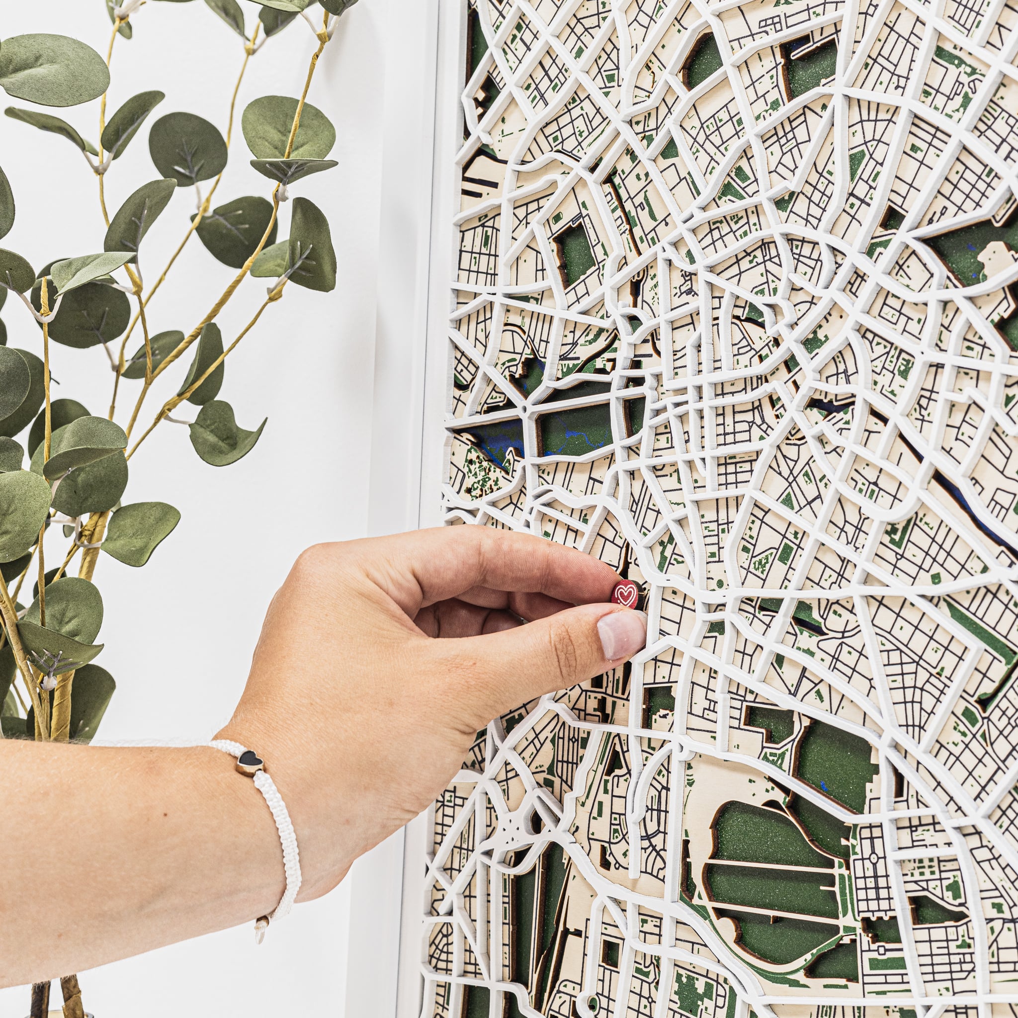 Hand holding a cut-out city map against a white wall with greenery.
