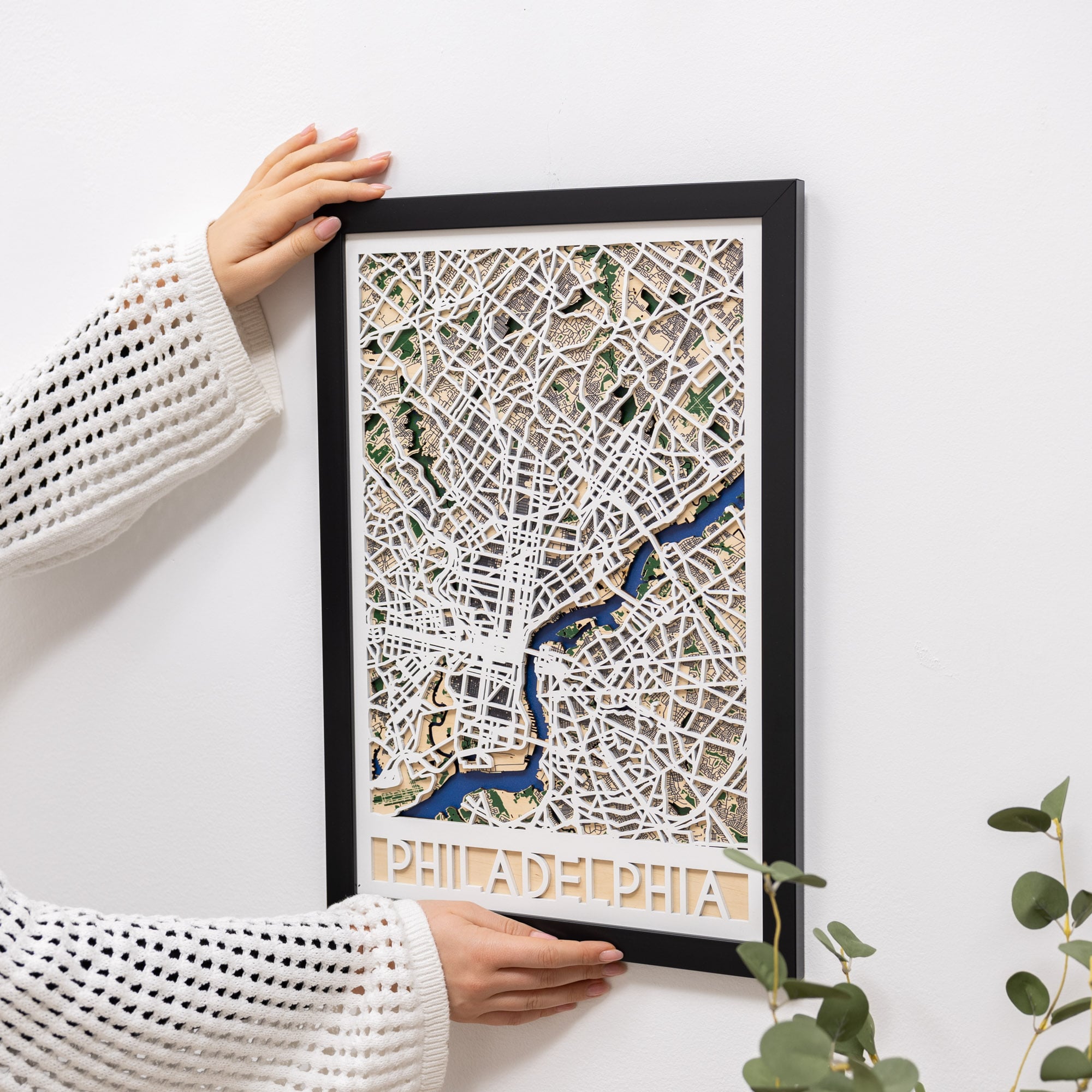 Framed map of Philadelphia held by a person against a white wall.
