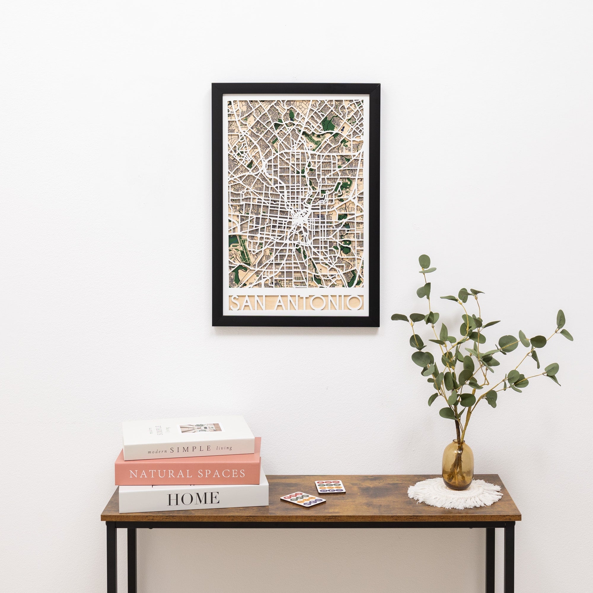 Framed map of San Antonio on a wall above a wooden table with books and a plant.
