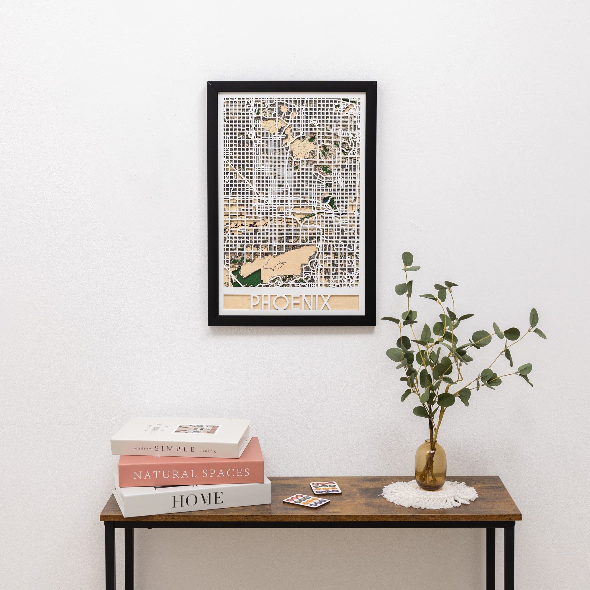 Framed map of Phoenix on a wall above a wooden table with books and a plant.