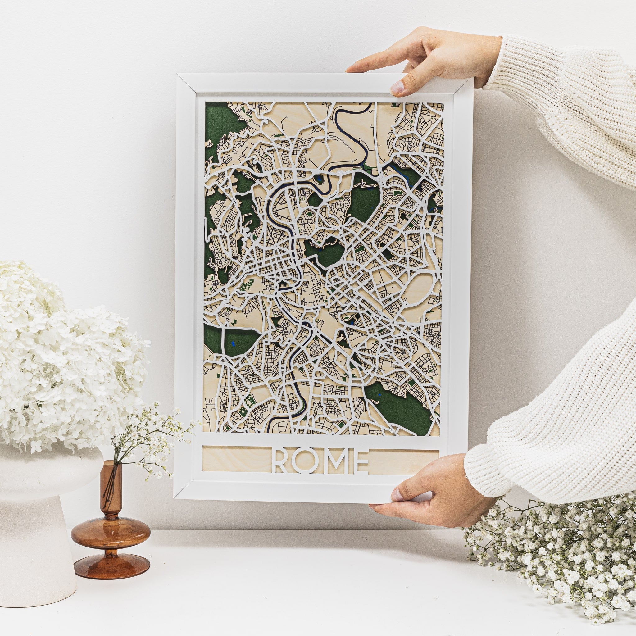 Framed map of Rome held by a person on a white surface with decorative elements.