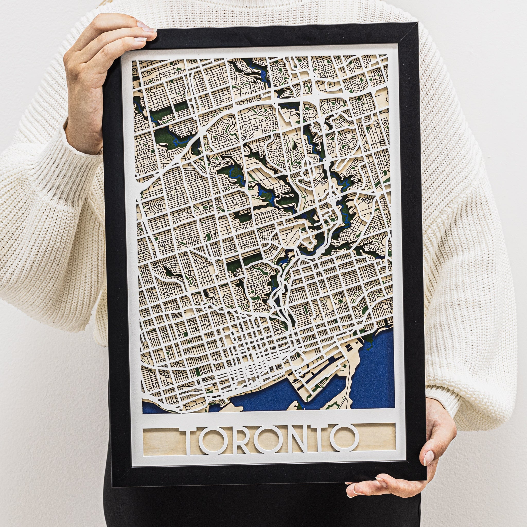 Framed map of Toronto held by a person wearing a white sweater.
