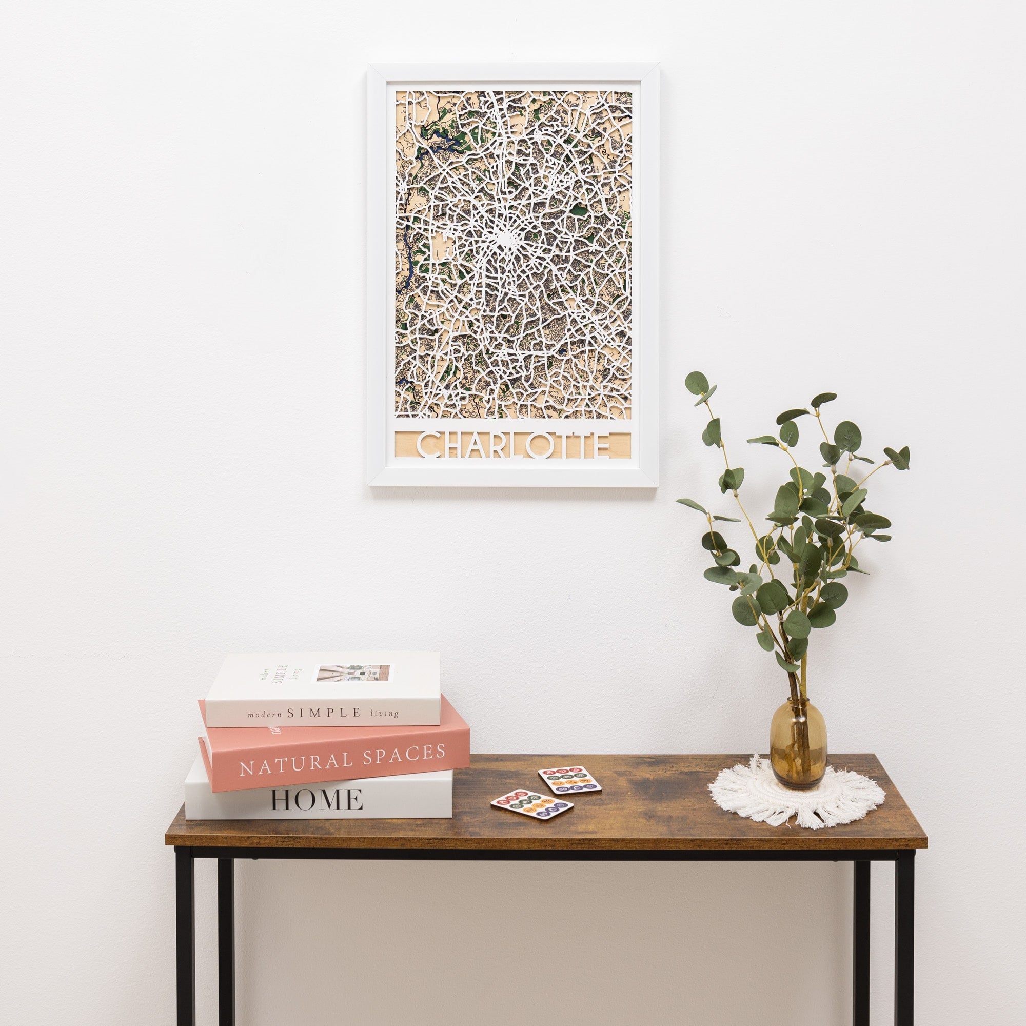 Framed artwork on a wall above a wooden console table with books and a vase.