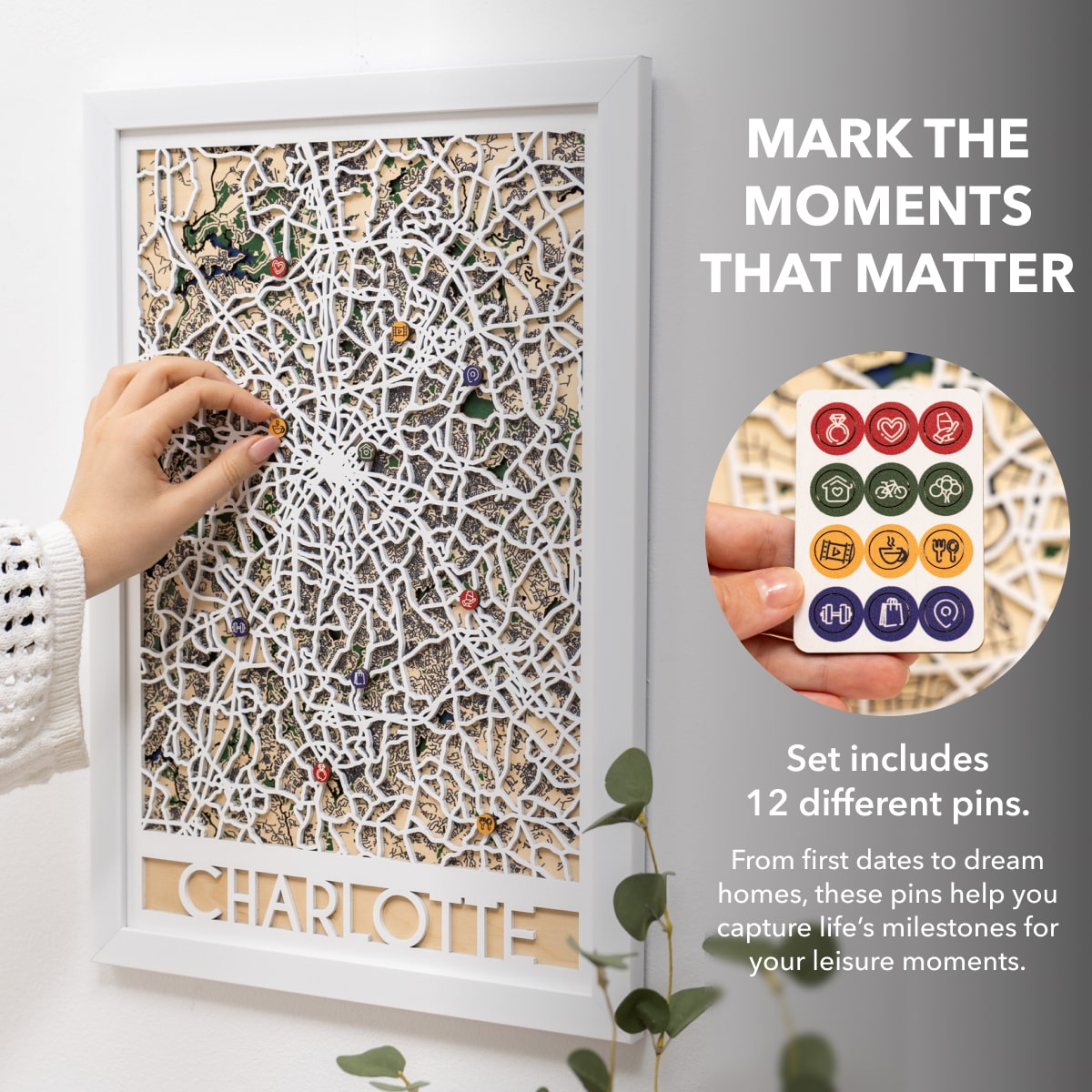 Decorative wall art with a hand placing a pin, accompanied by a set of pins and text about marking life's milestones.