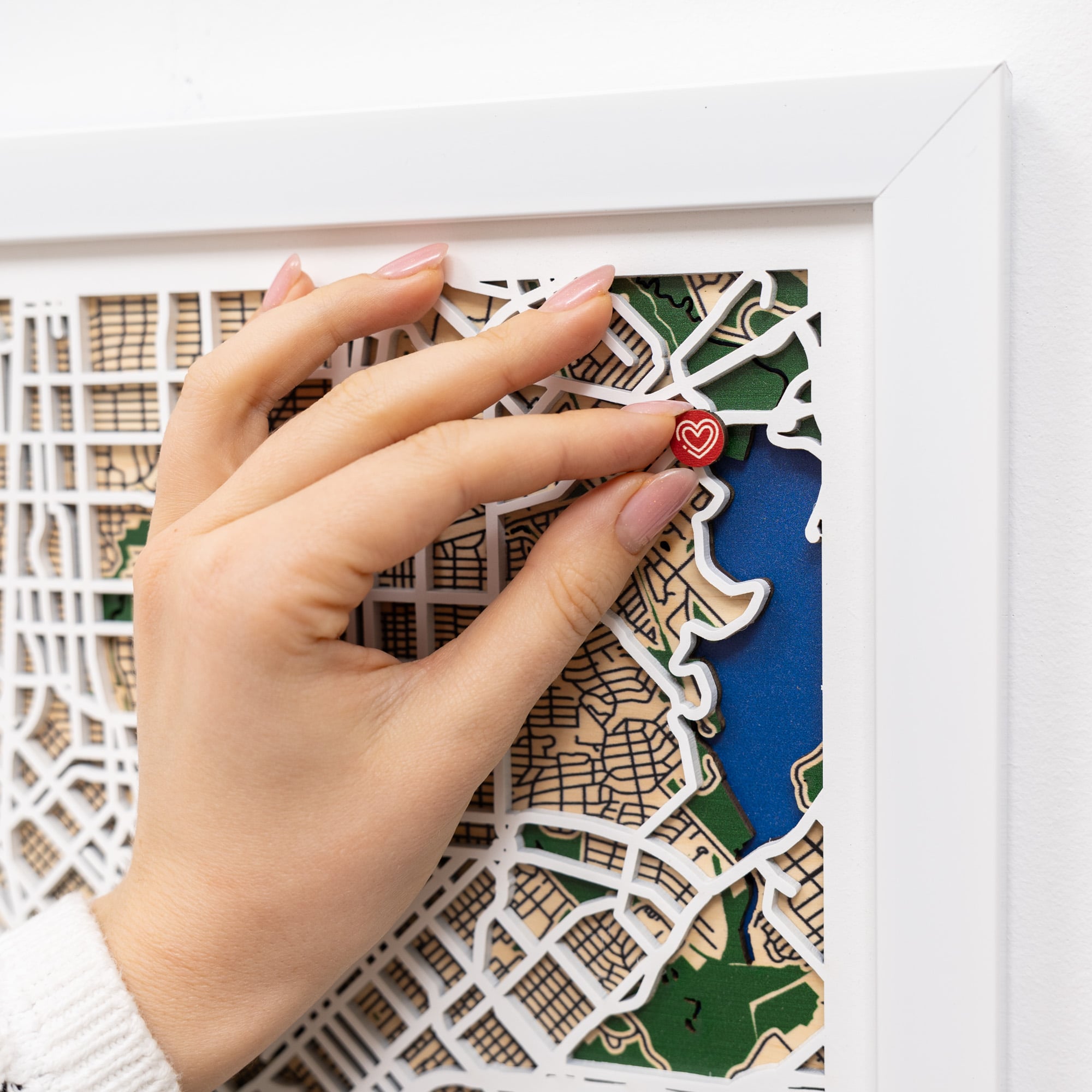 Hand placing a heart-shaped object on a decorative map in a white frame.