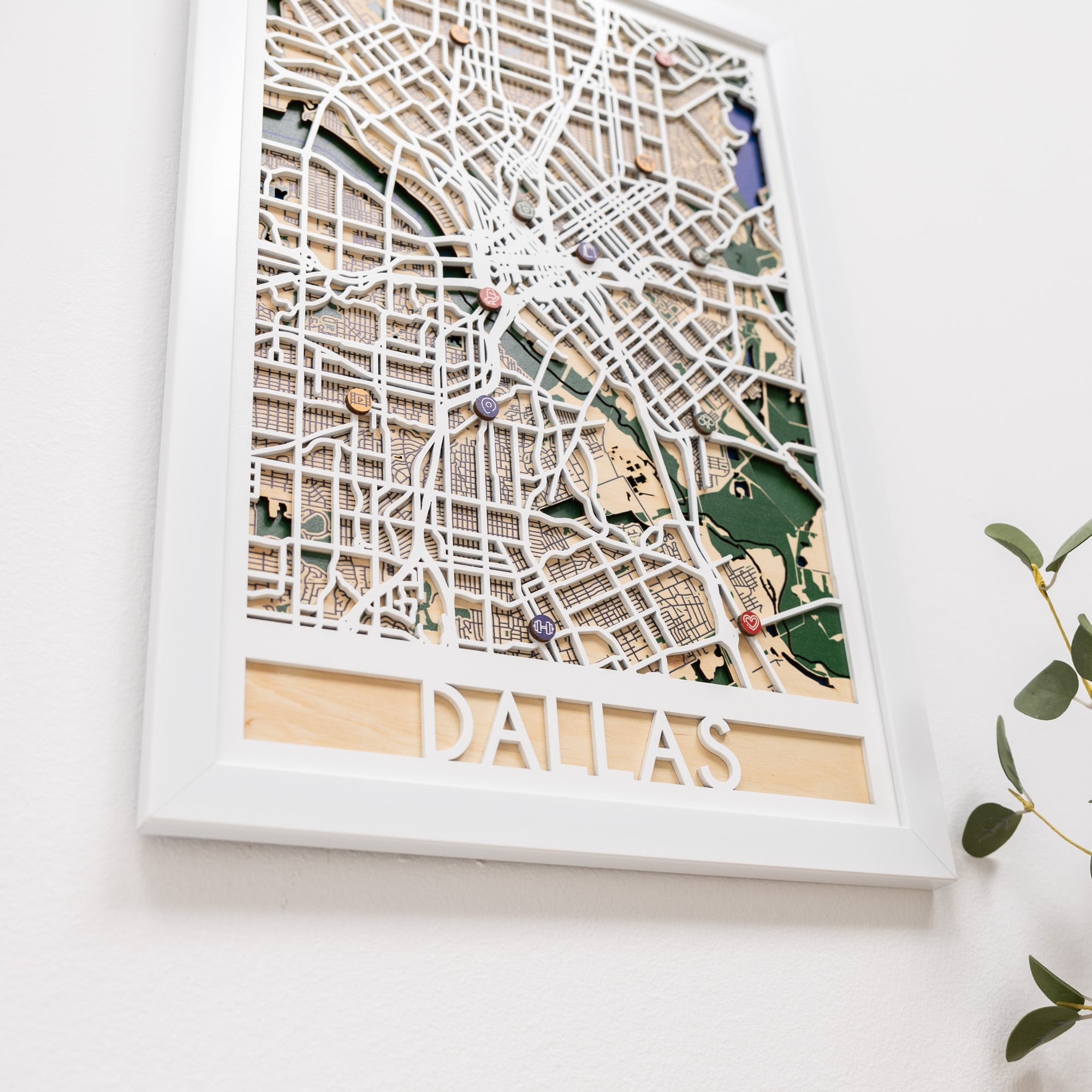 Woman hanging a framed map on a wall next to a wooden side table with books and a plant.