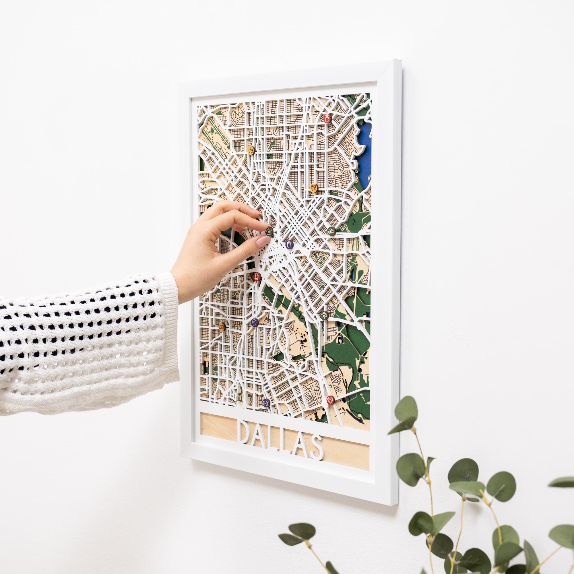 Woman hanging a framed map on a wall next to a wooden side table with books and a plant.