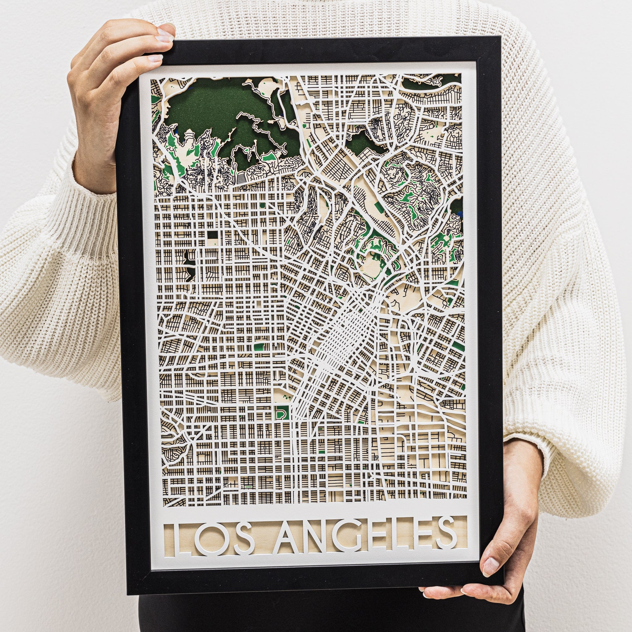 Framed map of Los Angeles held by a person wearing a white sweater.