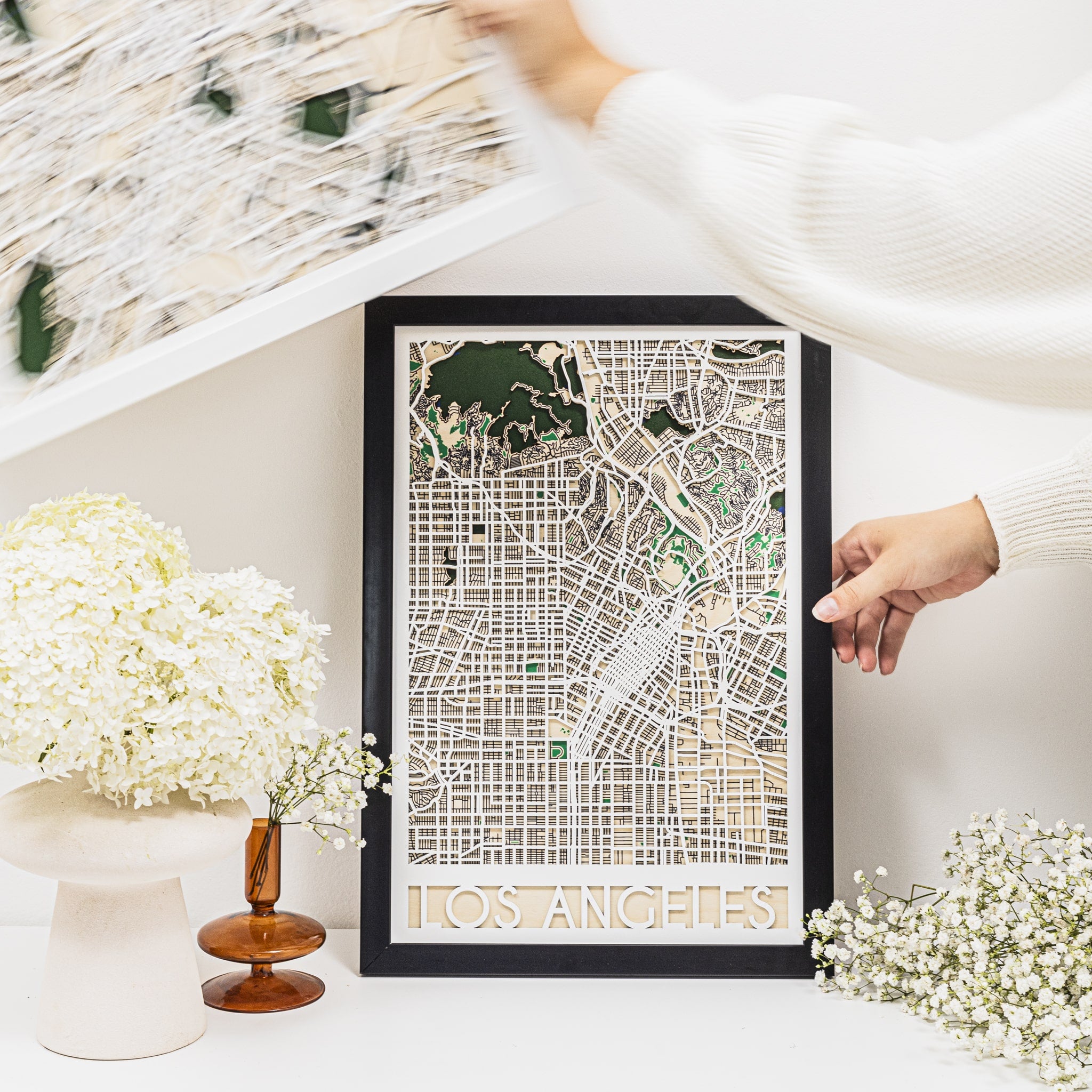 Framed city map of Los Angeles on a decorative shelf with flowers.