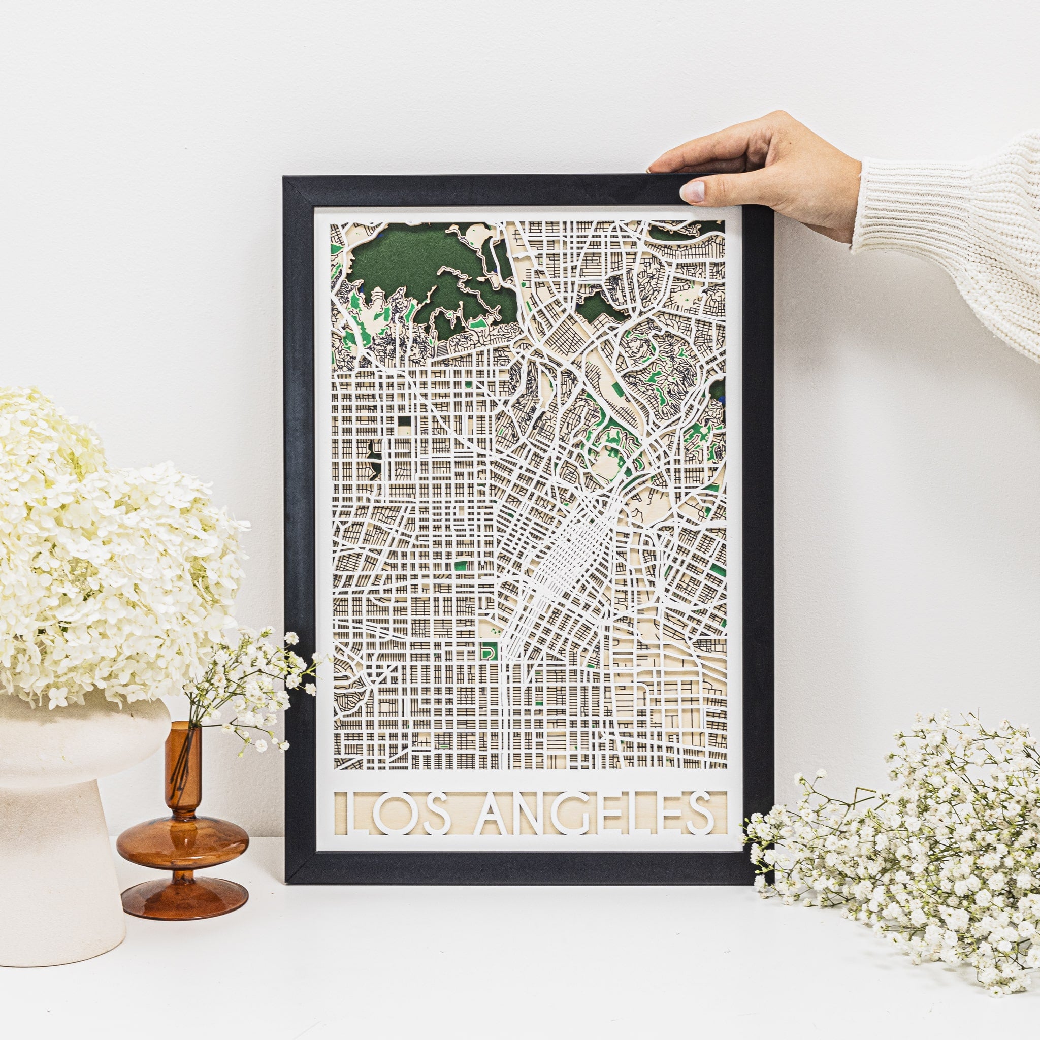 Framed map of Los Angeles held by a hand on a white surface with flowers.