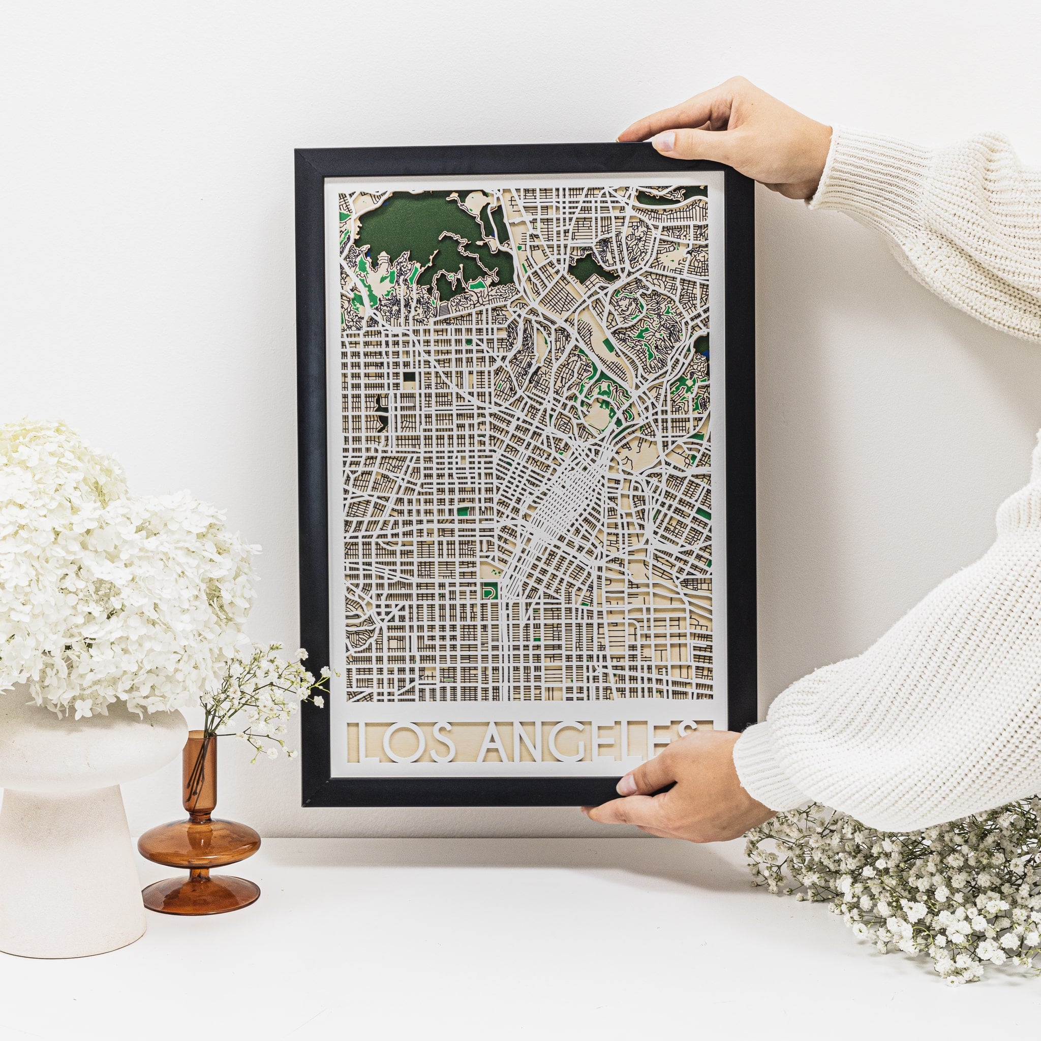 Person holding a framed map of Los Angeles on a white surface with decorative elements.