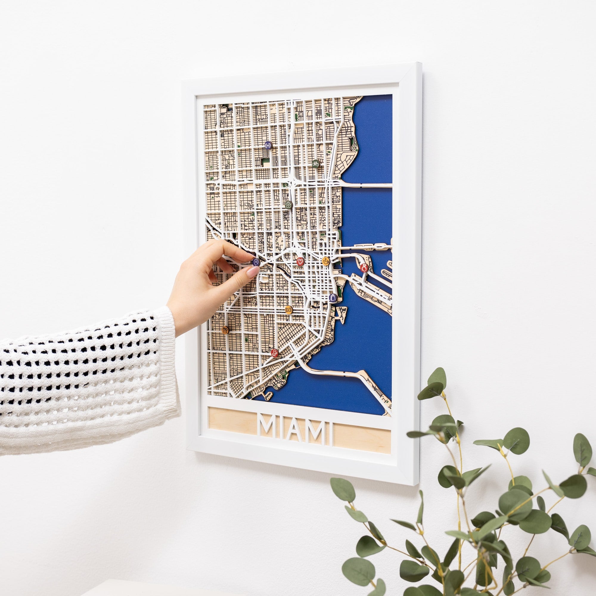 Framed city map of Miami held by a hand on a white surface with a plant in the corner.