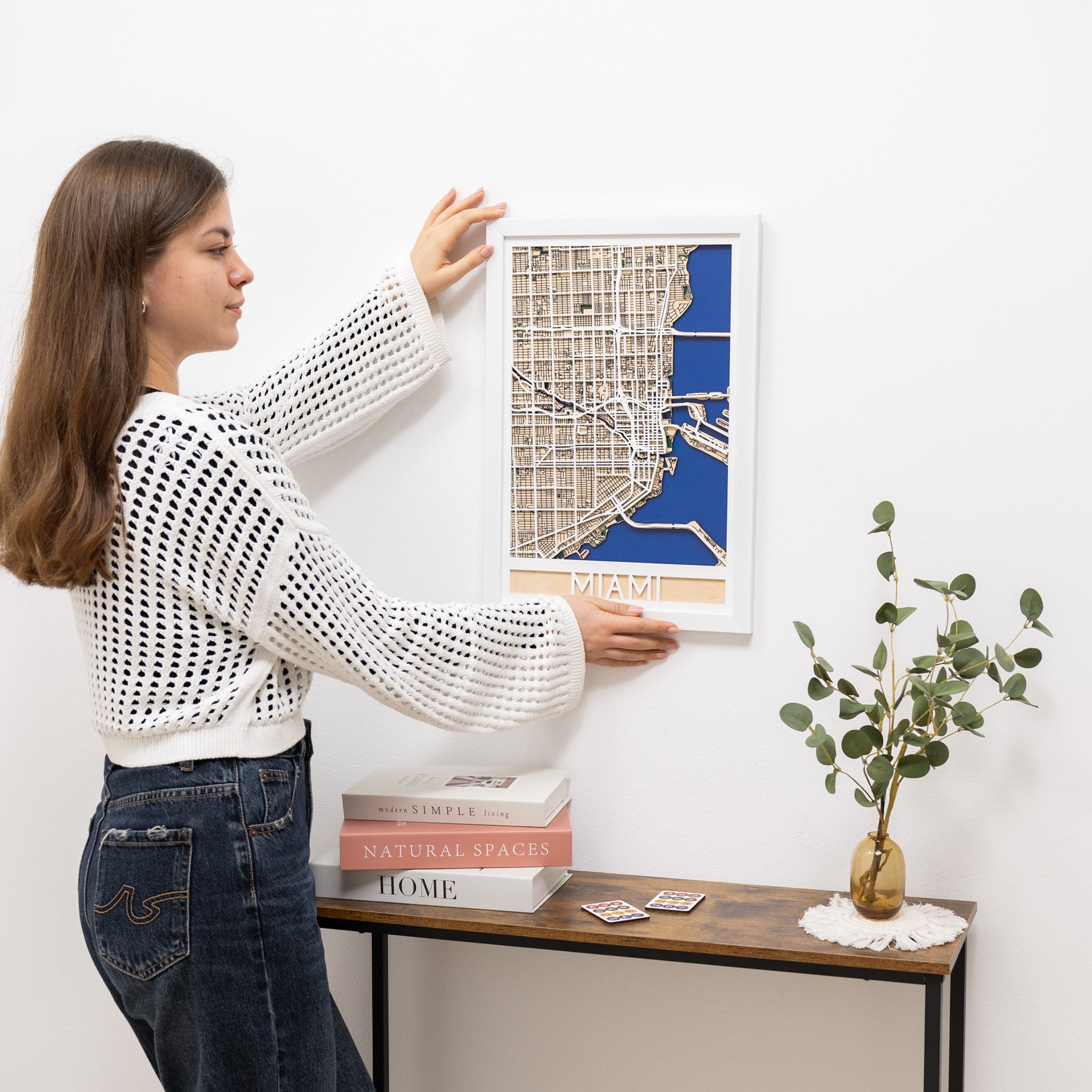 Woman hanging a framed map of Miami on a wall