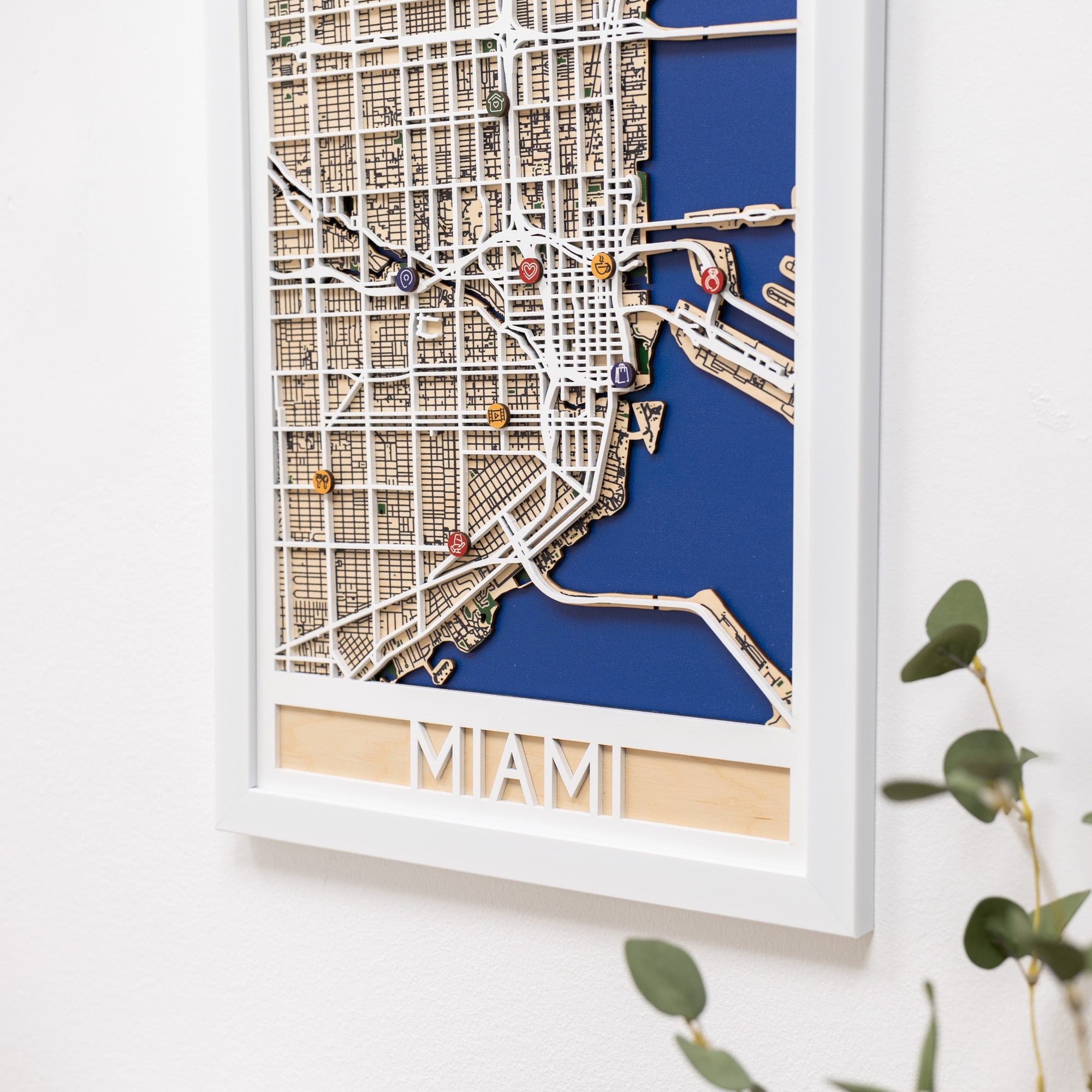 Framed map of Miami with decorative pins on a white wall.