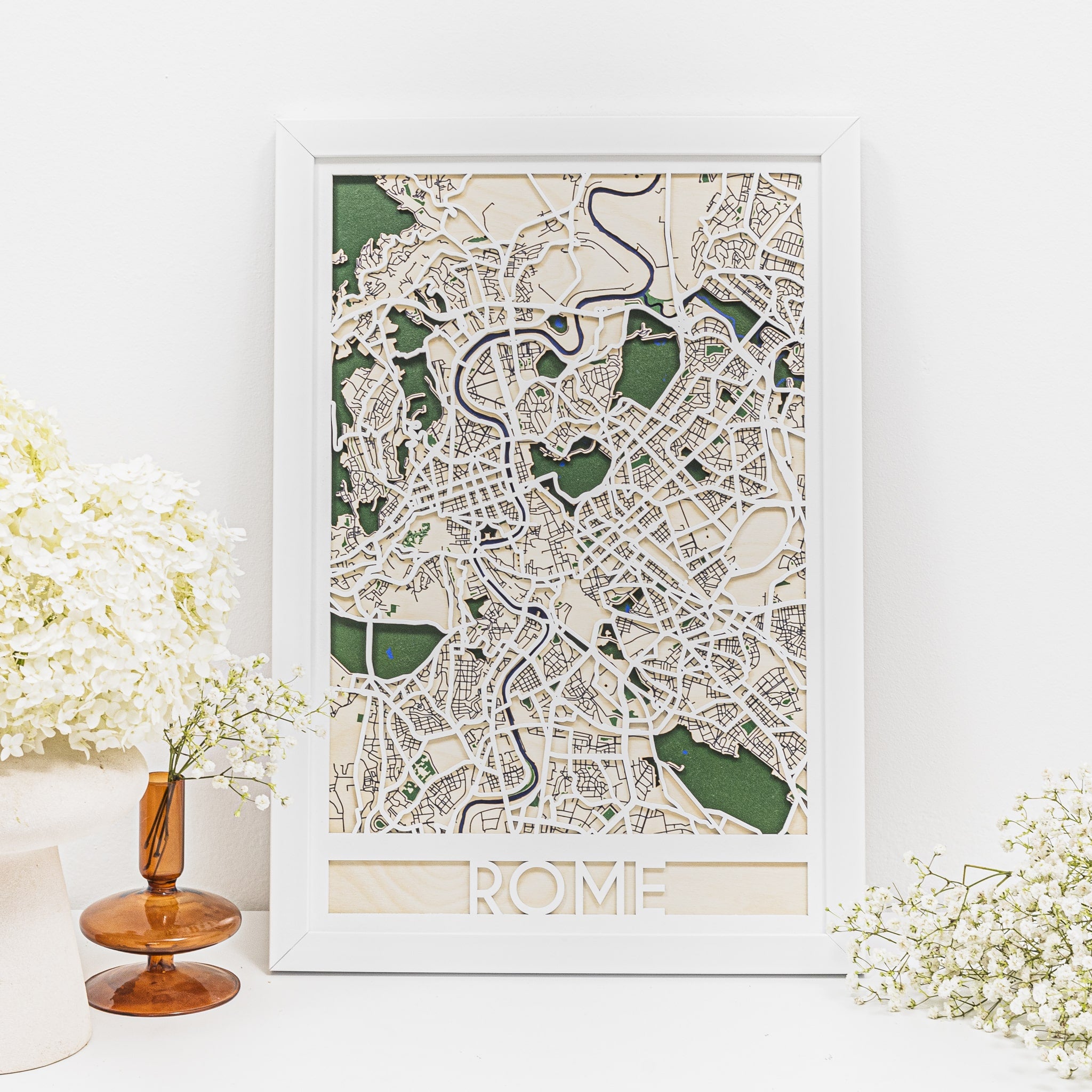 Framed map of Rome on a white wall with decorative elements.