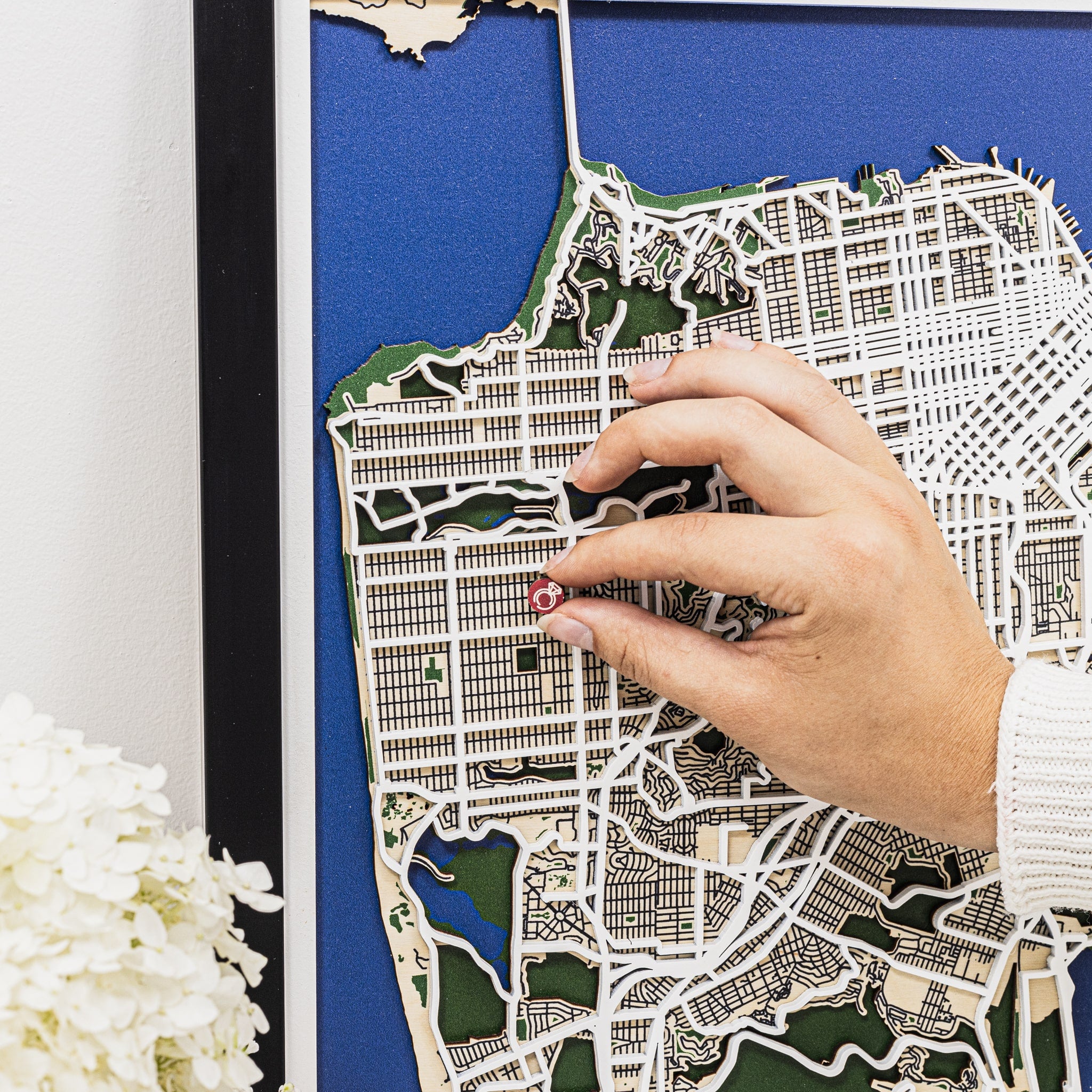 Hand placing a red pin on a detailed map of a city with a blue background