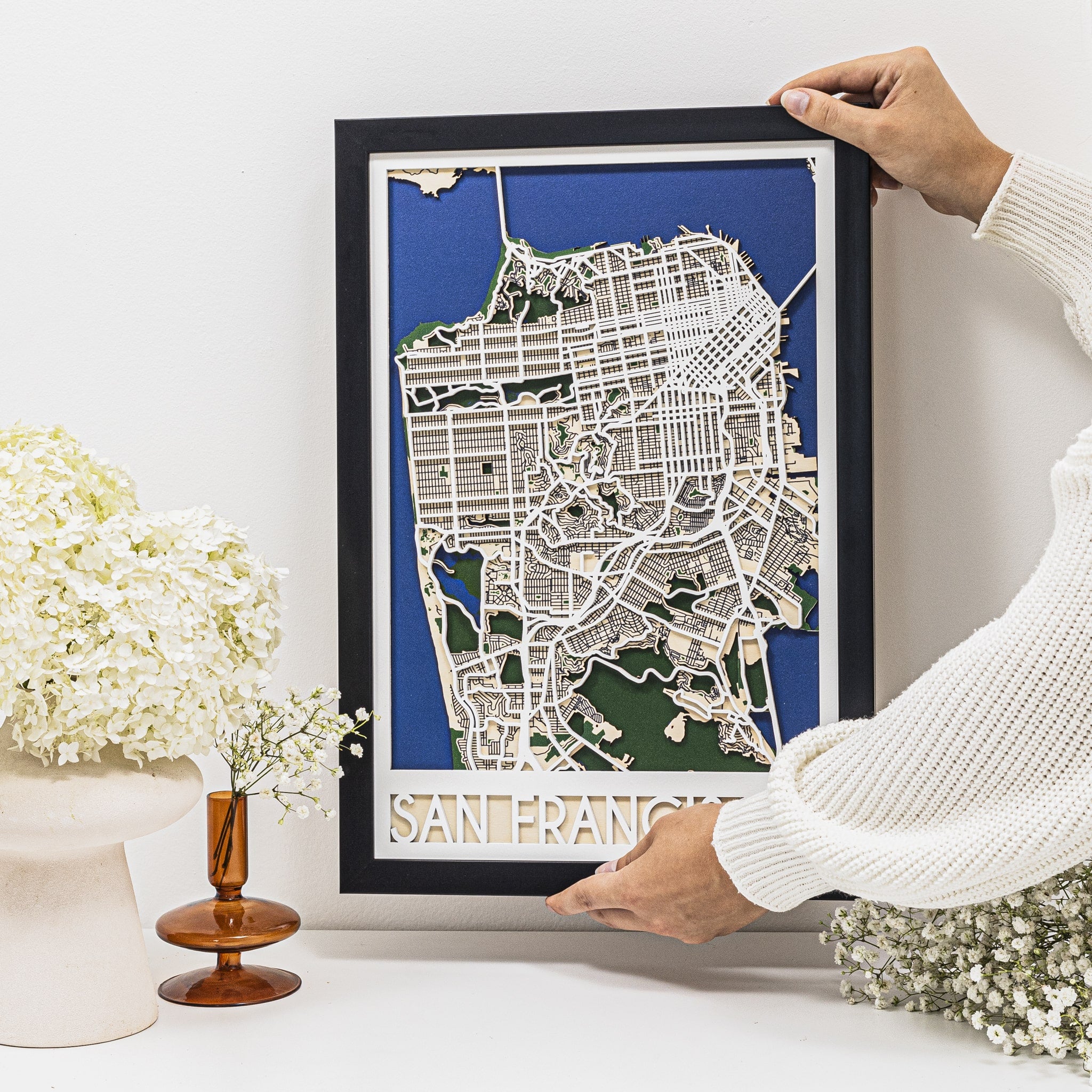 Framed map of San Francisco held by a person with decorative elements in the background