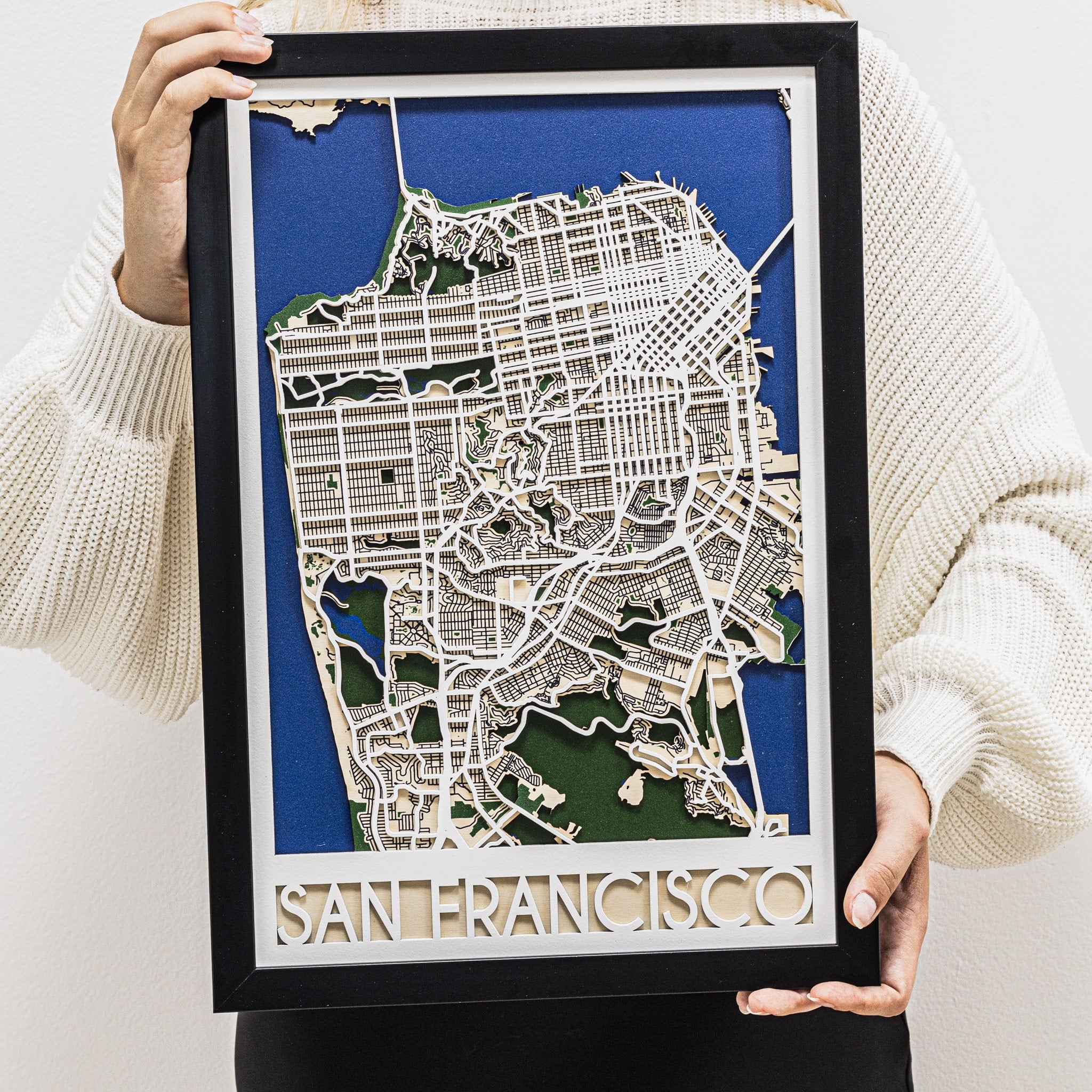Framed map of San Francisco held by a person wearing a beige sweater.