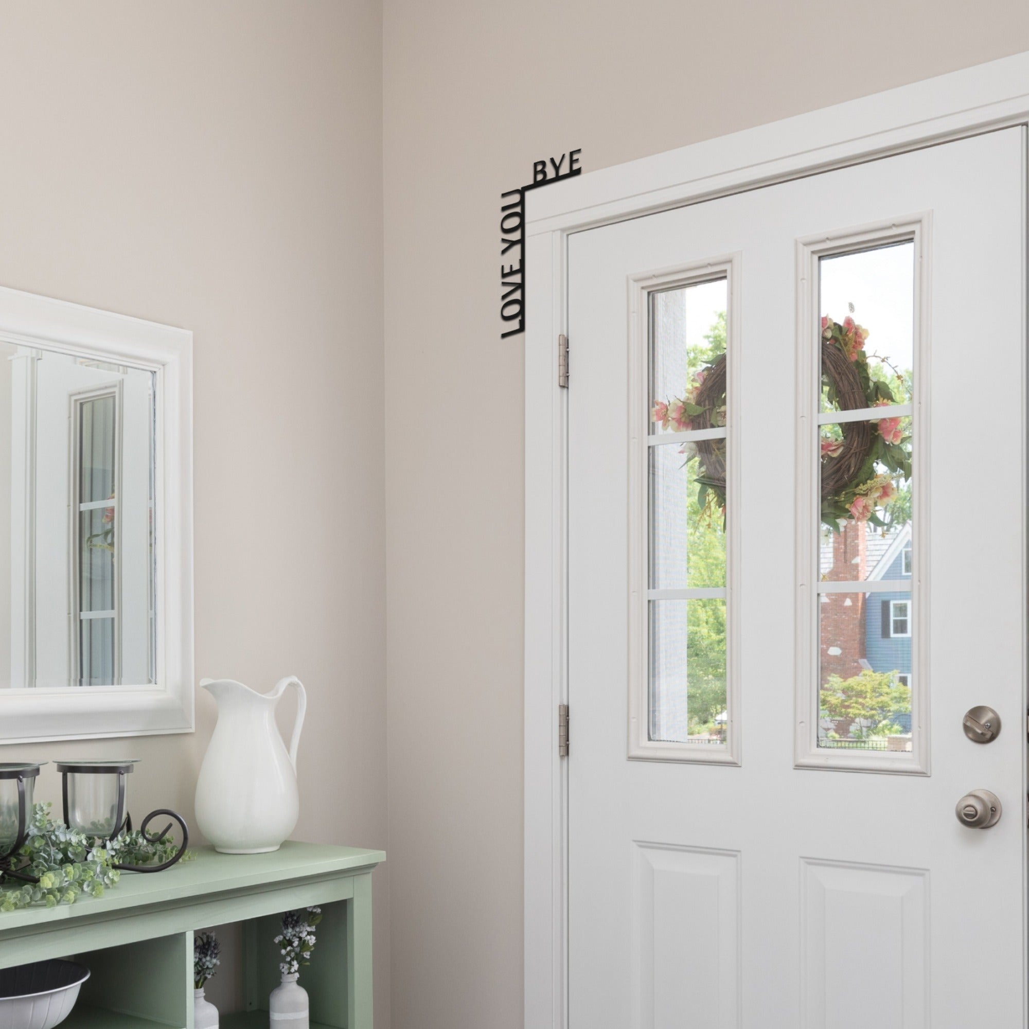 White door with wreath, light green console table with decorative items, and wall art.