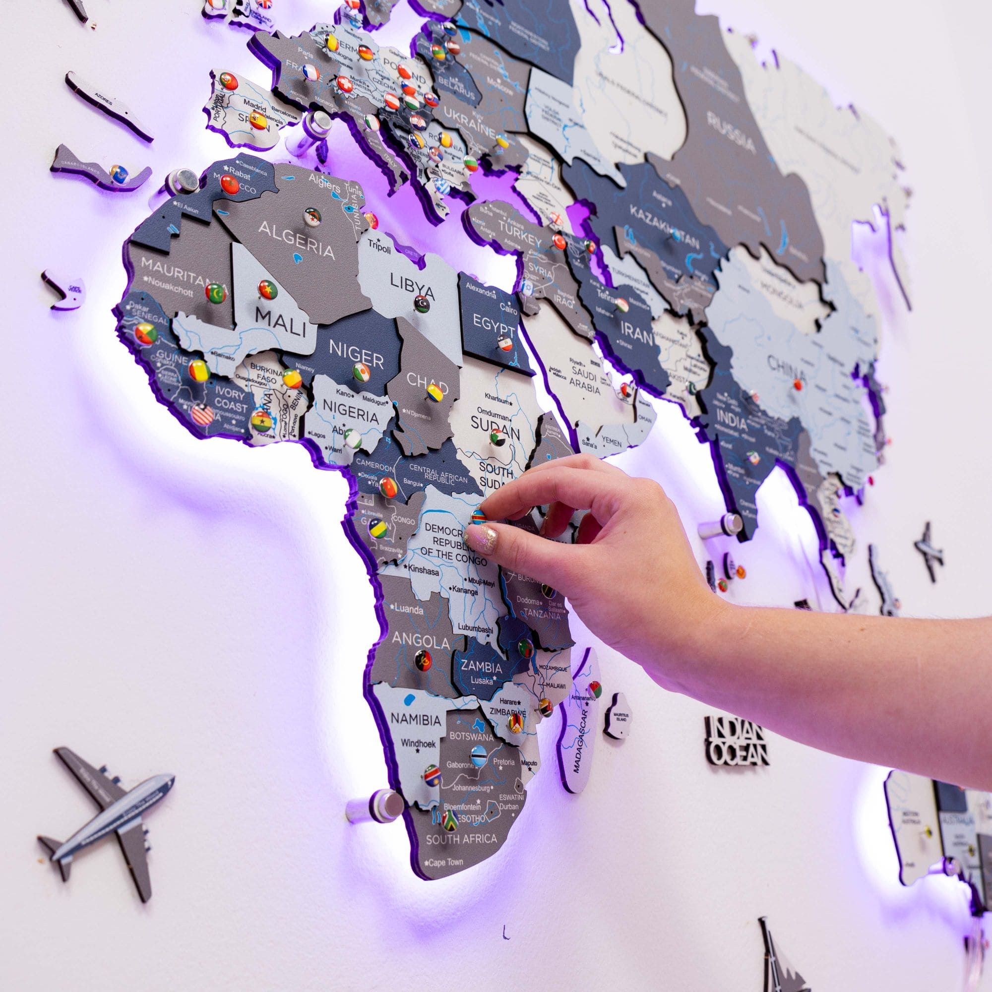 World map with illuminated edges, hand placing a marker on Africa, airplane model below.