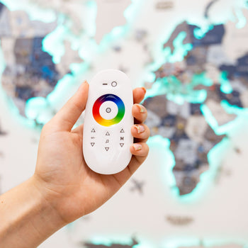 Hand holding a white remote control with color wheel and symbols against a blurred colorful background