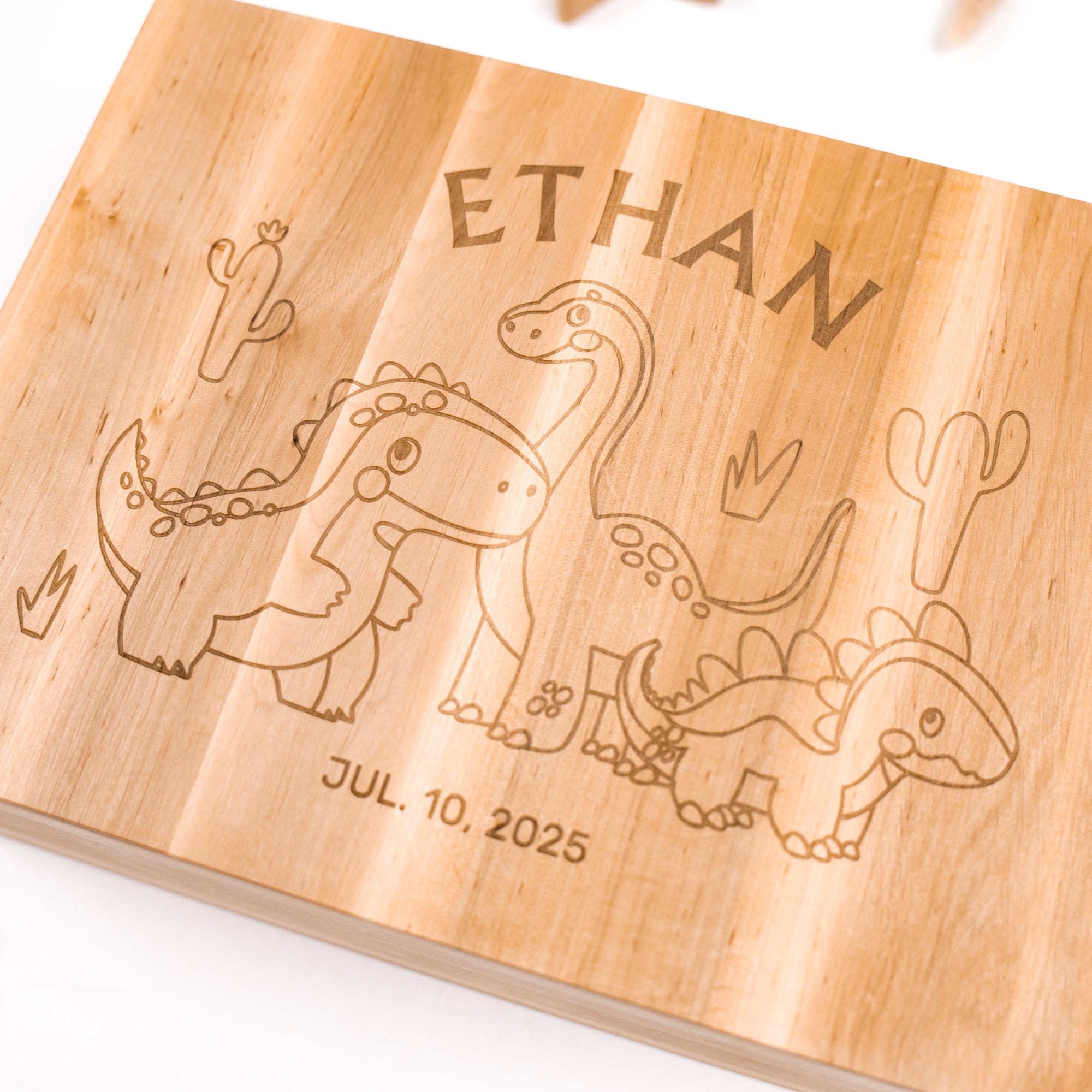 Wooden board with engraved dinosaur illustrations and the name 'Ethan' along with a date.