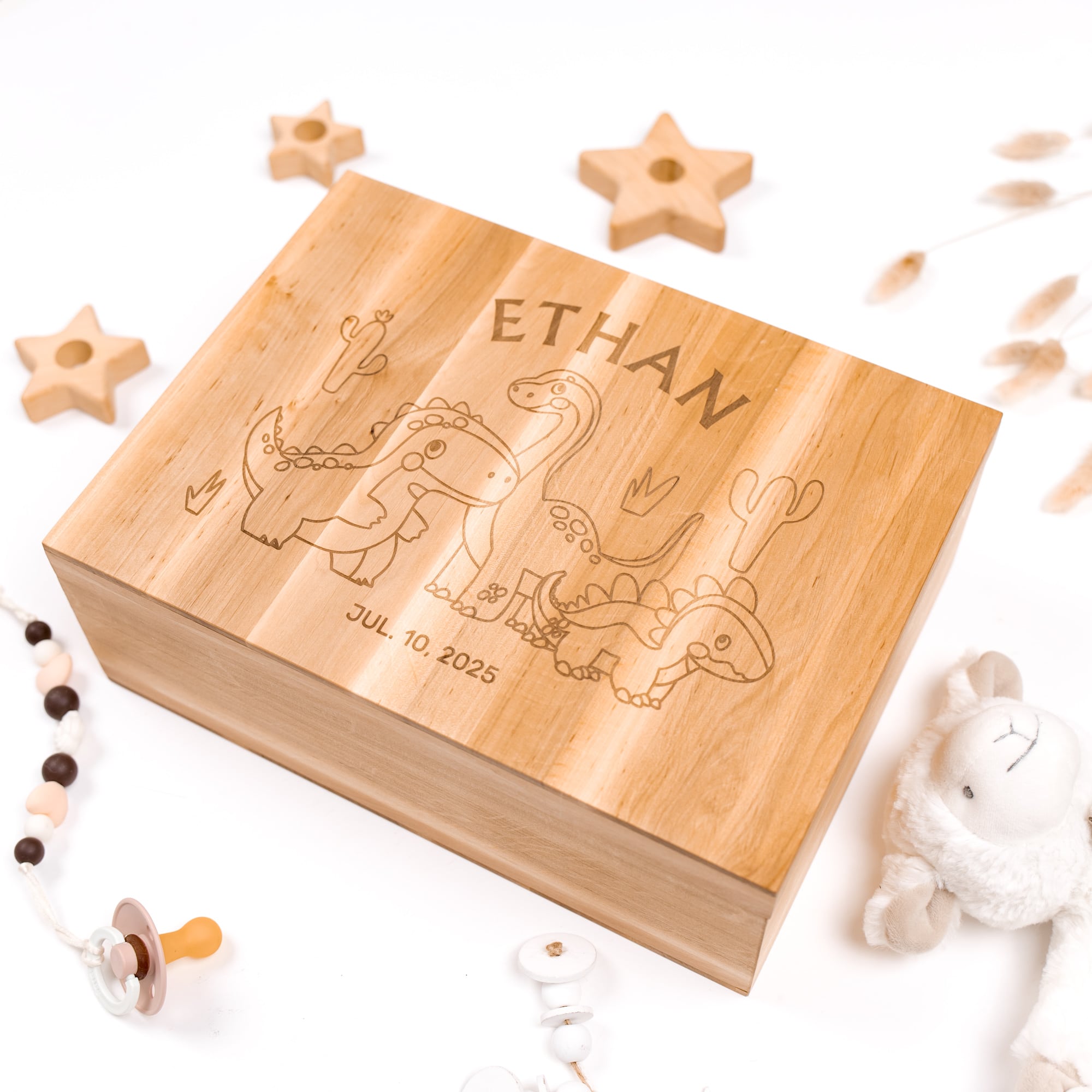 Wooden box engraved with 'Ethan' and baby illustrations, surrounded by baby toys on a white background.