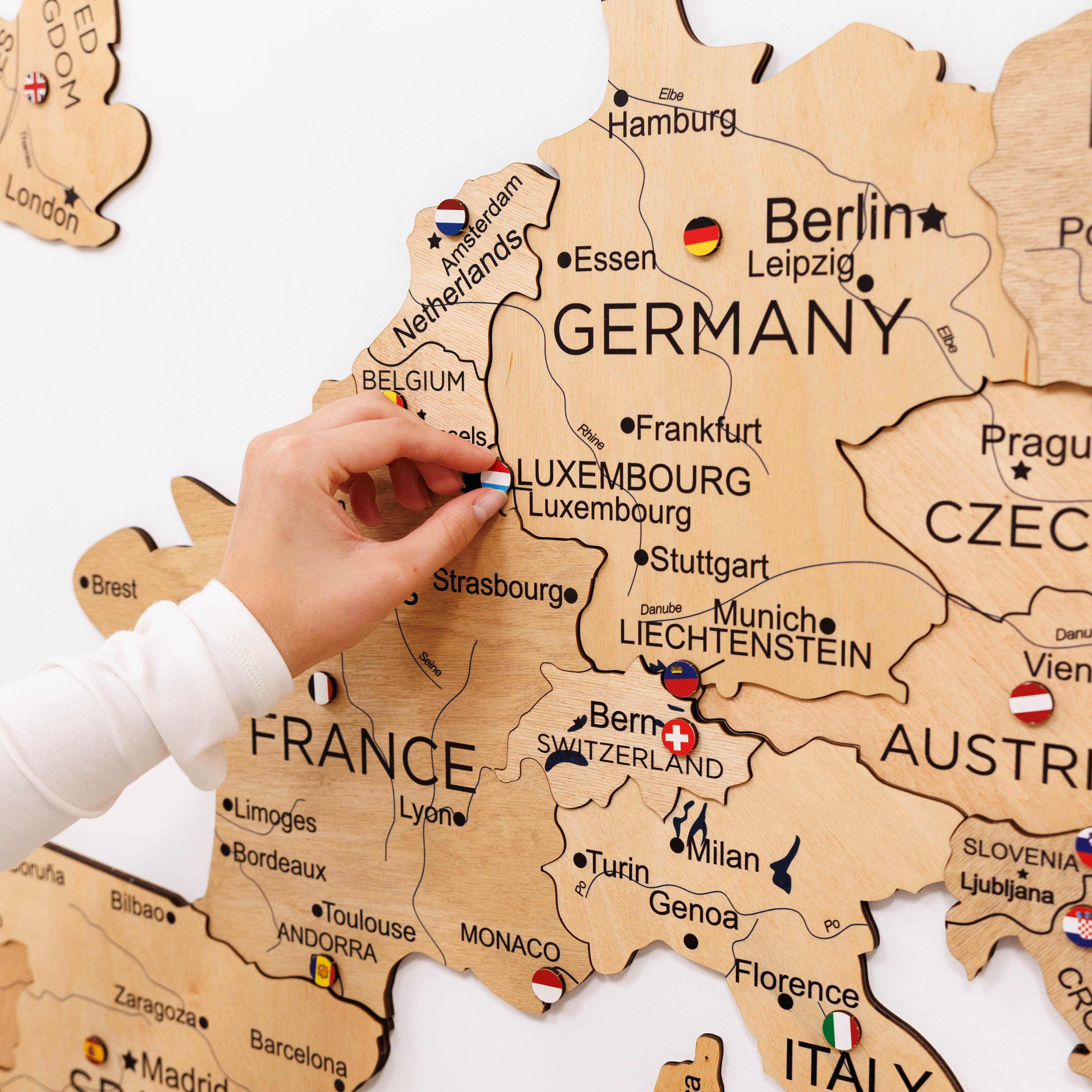 Wooden map of Europe with a hand placing a small flag on Germany.