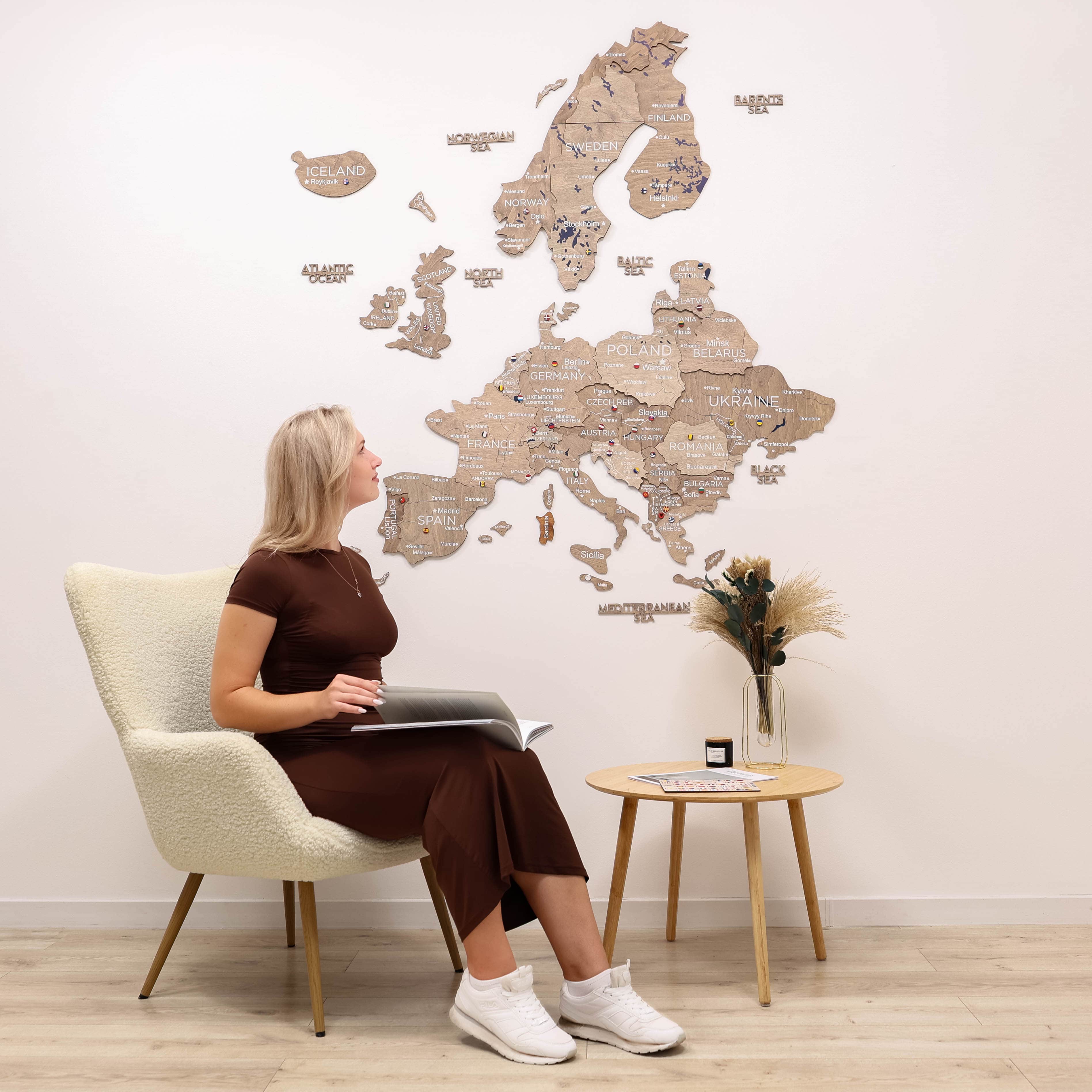 Woman sitting in a chair looking at a wooden world map on the wall.