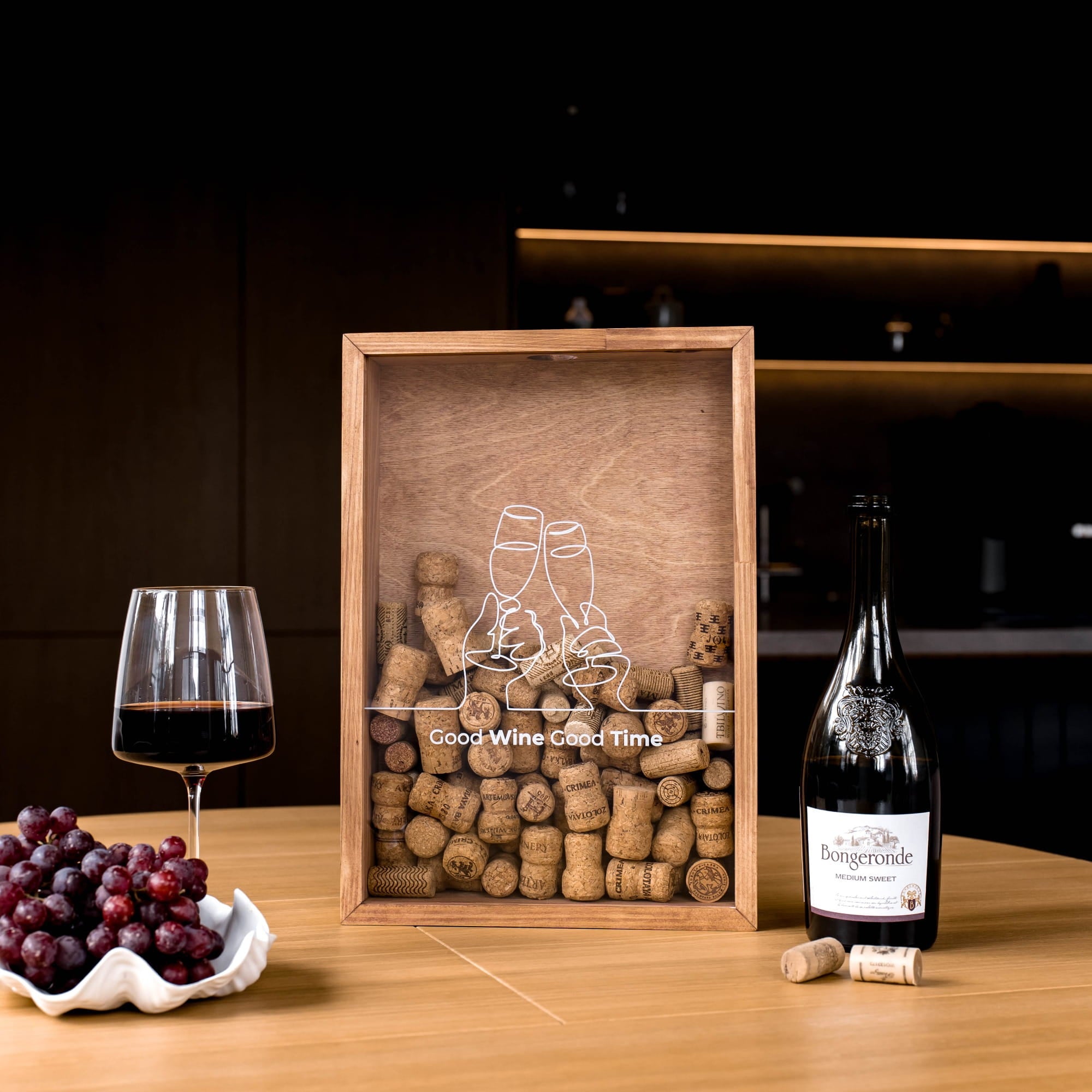 A wooden wine cork display box with an etched clinking glasses design