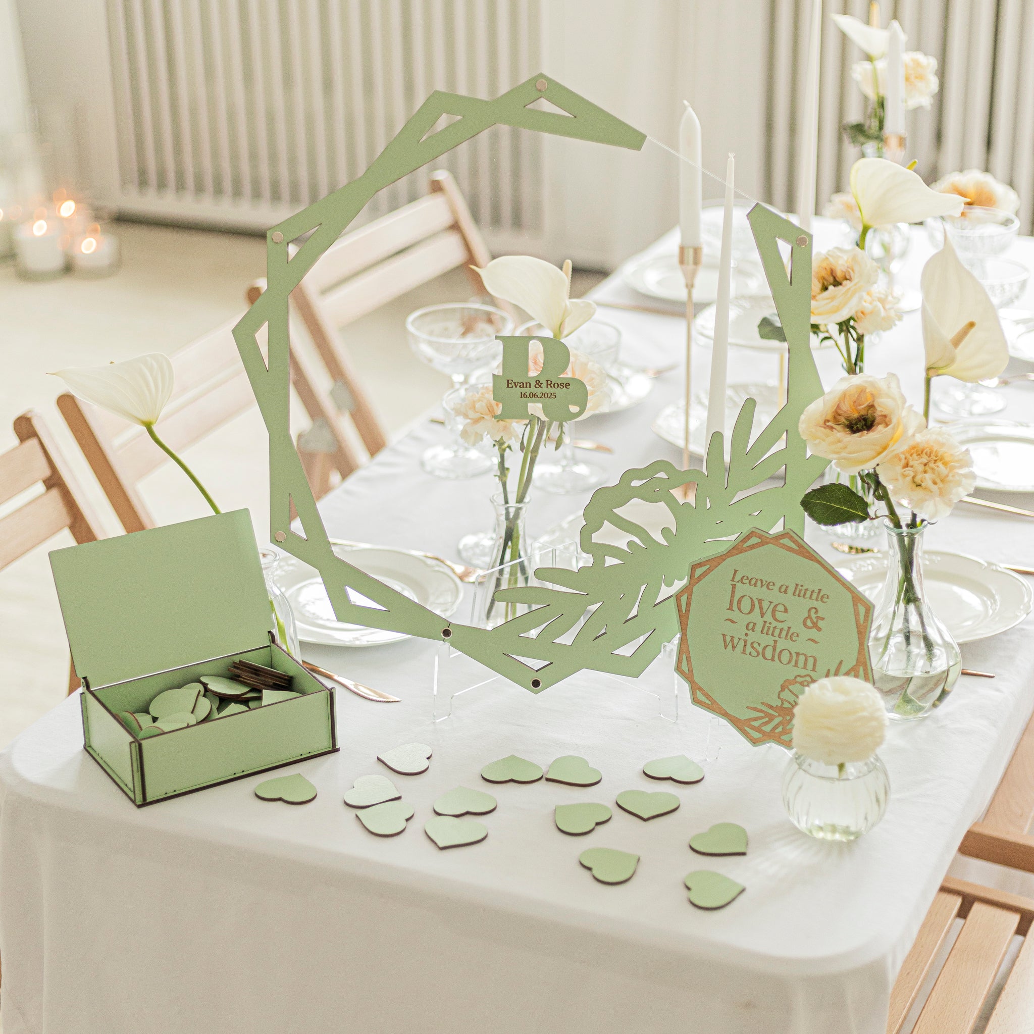Decorative table setting with green cut-out shapes, candles, and flowers on a white tablecloth.