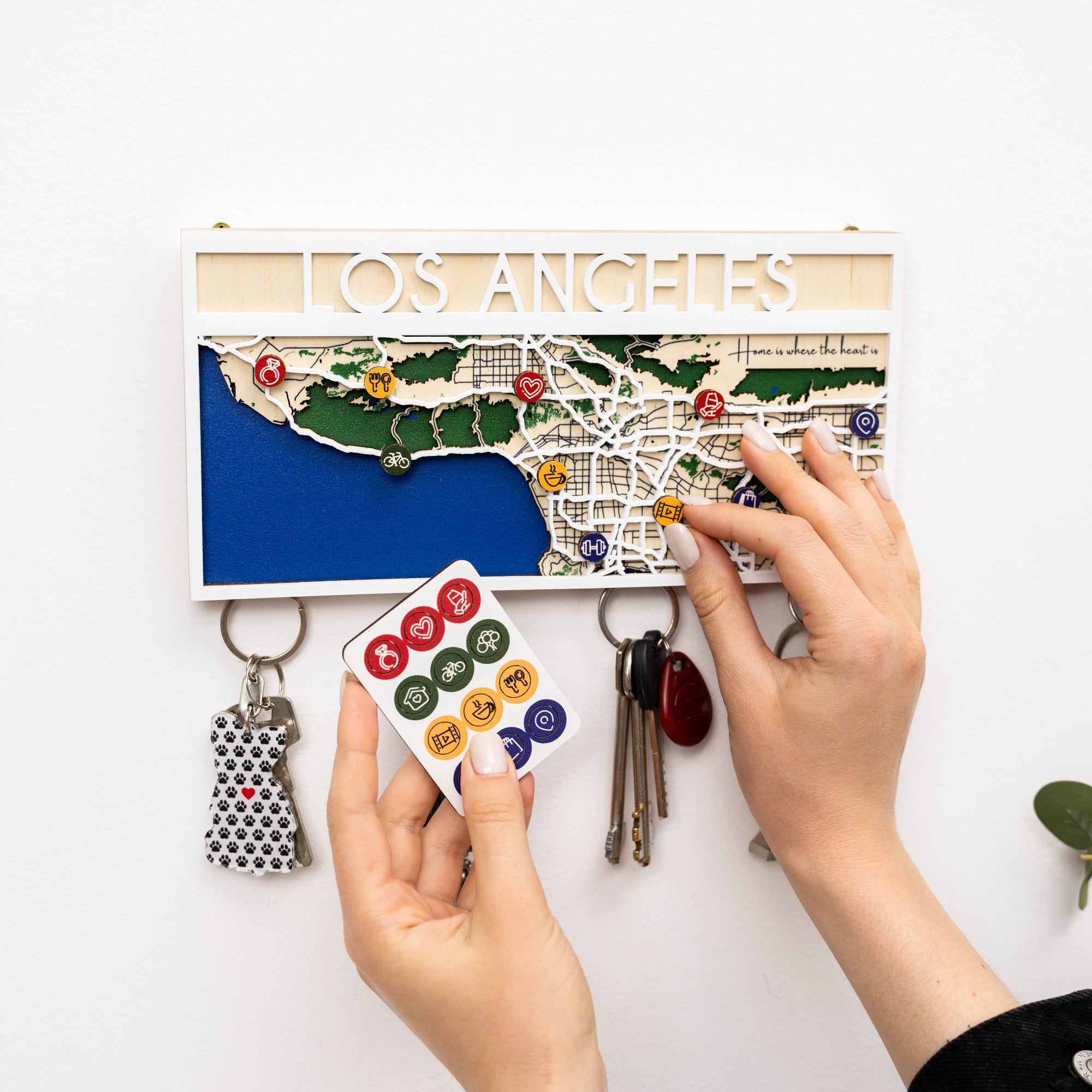 Person using a keychain holder with a map of Los Angeles and various keys and cards on a white background