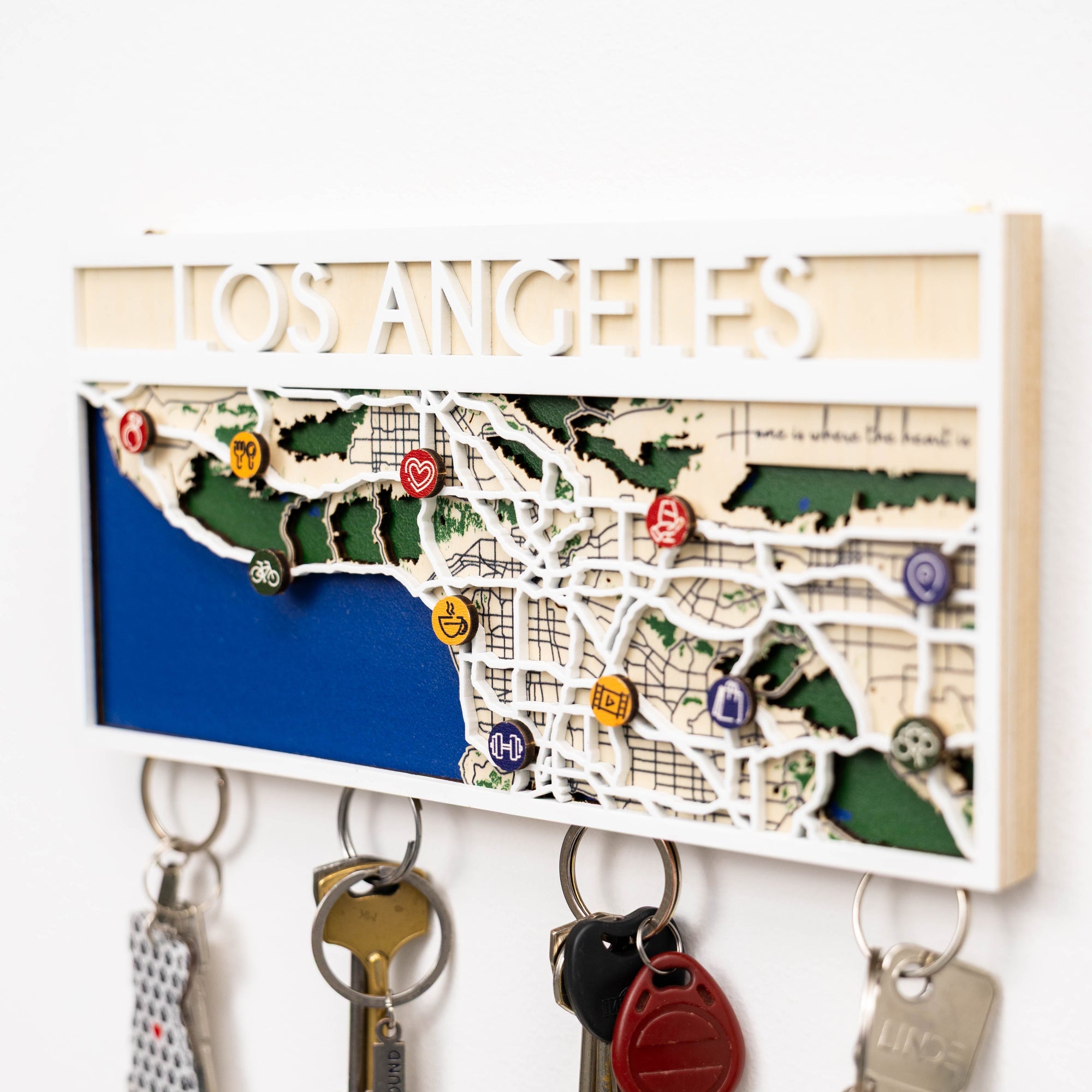 Key holder with a map of Los Angeles and decorative pins on a white wall.