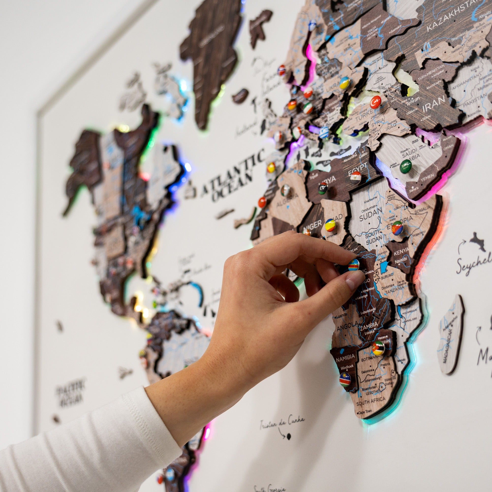 Hand placing a pin on a world map with colorful pins on a white wall.